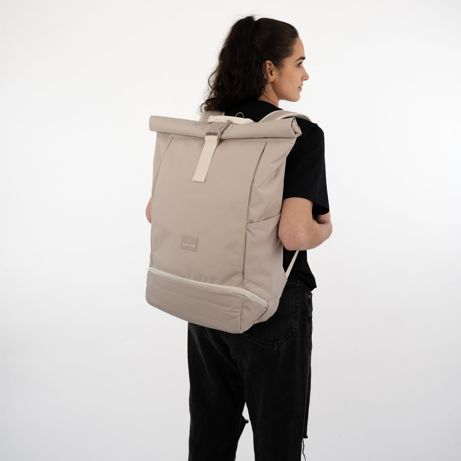 Frau trägt beigen Rolltop Rucksack Allen XL, von hinten, schwarzes T-Shirt und schwarze Hose