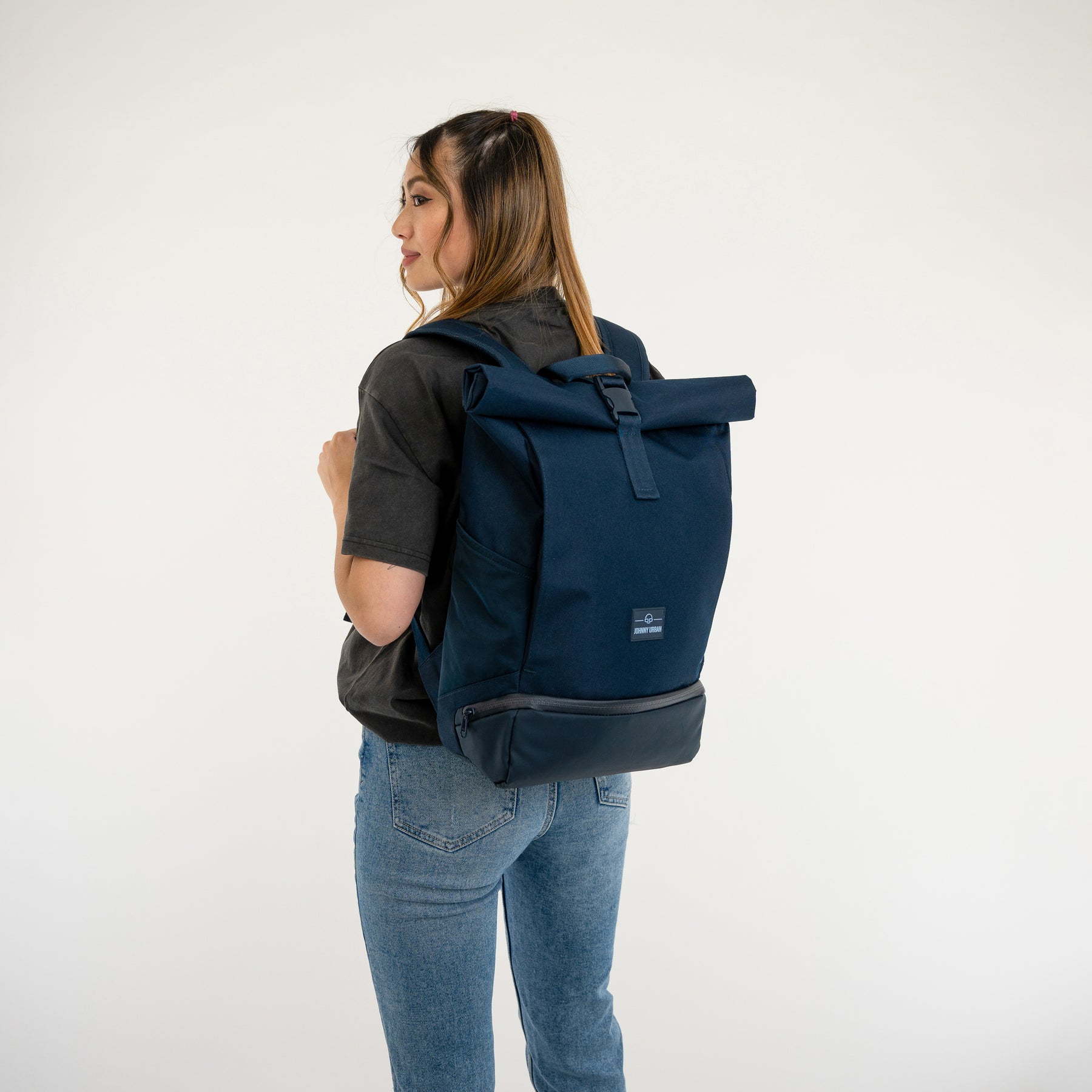 Frau trägt blauen Rolltop Rucksack Allen Medium von Johnny Urban mit schwarzem T-Shirt und blauen Jeans