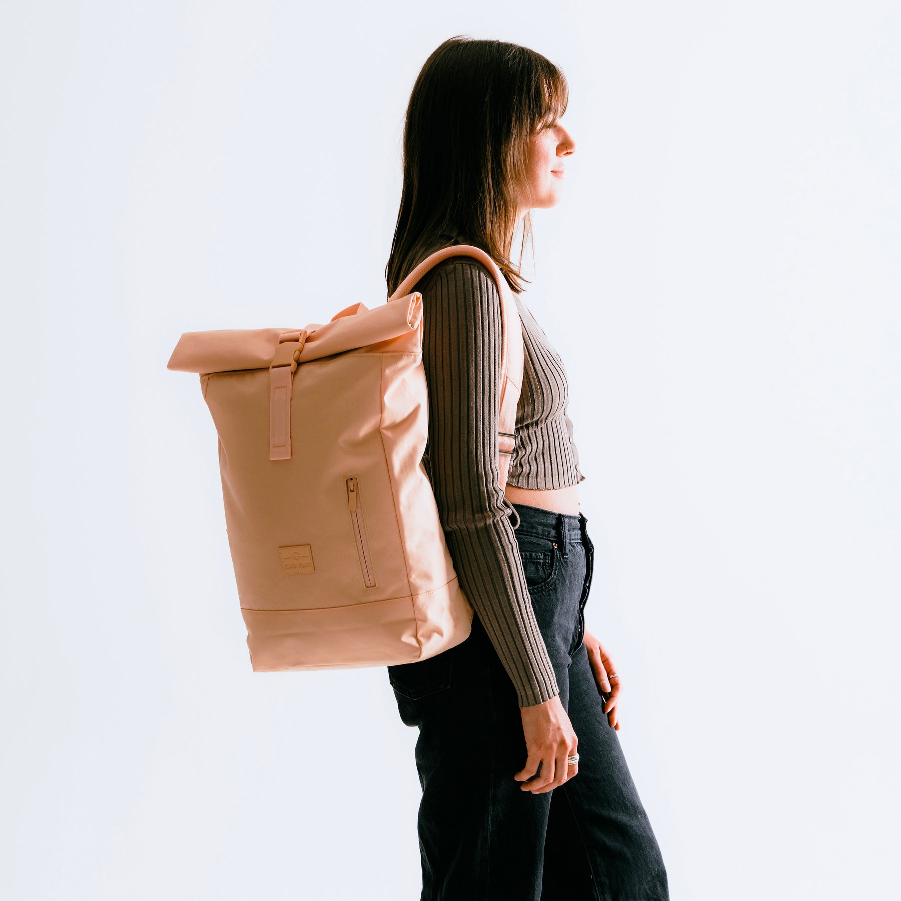 Frau trägt hellrosa Rolltop-Rucksack ‚Robin Medium‘ von Johnny Urban zu dunkler Hose und gestreiftem Oberteil