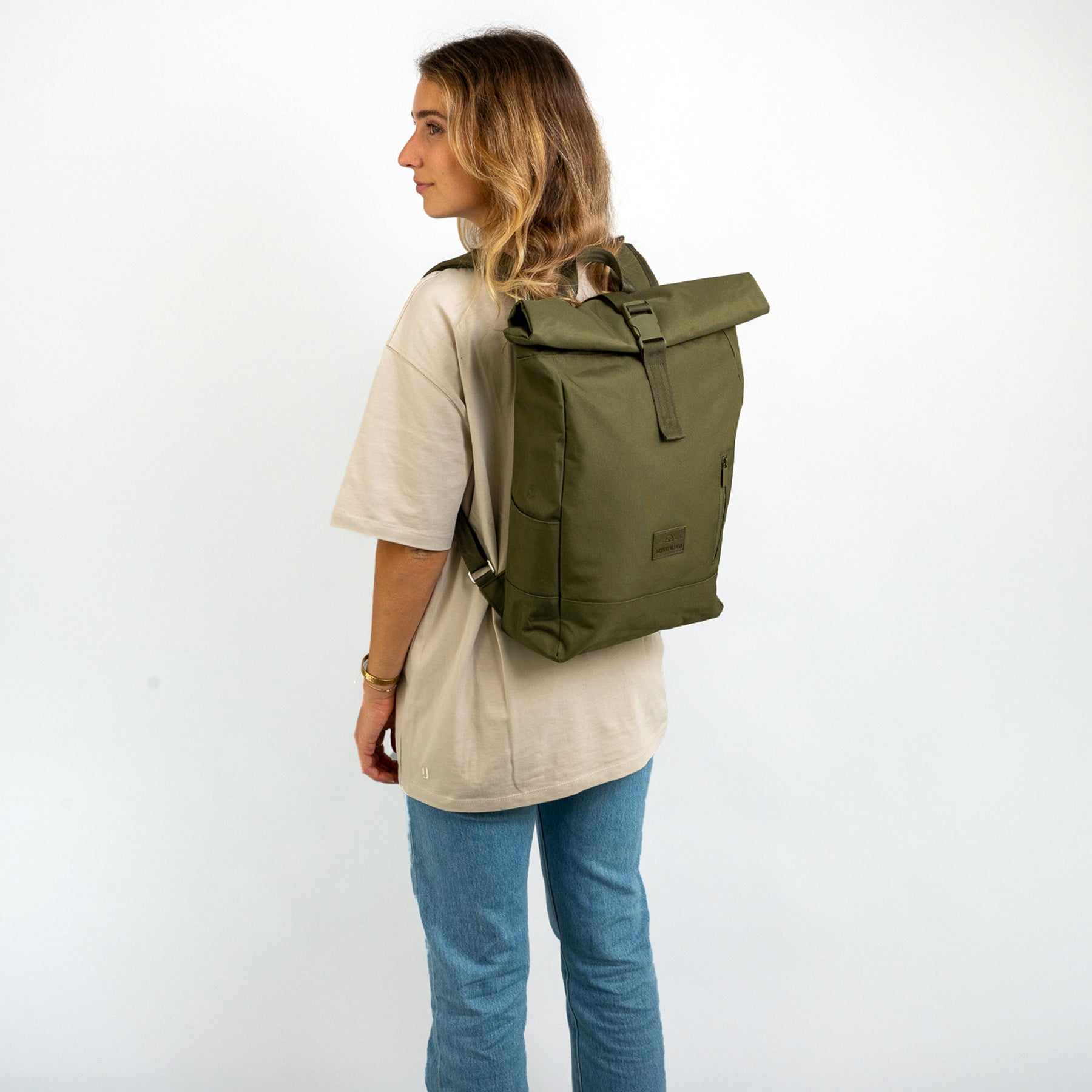 Frau trägt olivgrünen Rolltop Rucksack 'Robin Medium' von Johnny Urban, beige T-Shirt, blaue Jeans