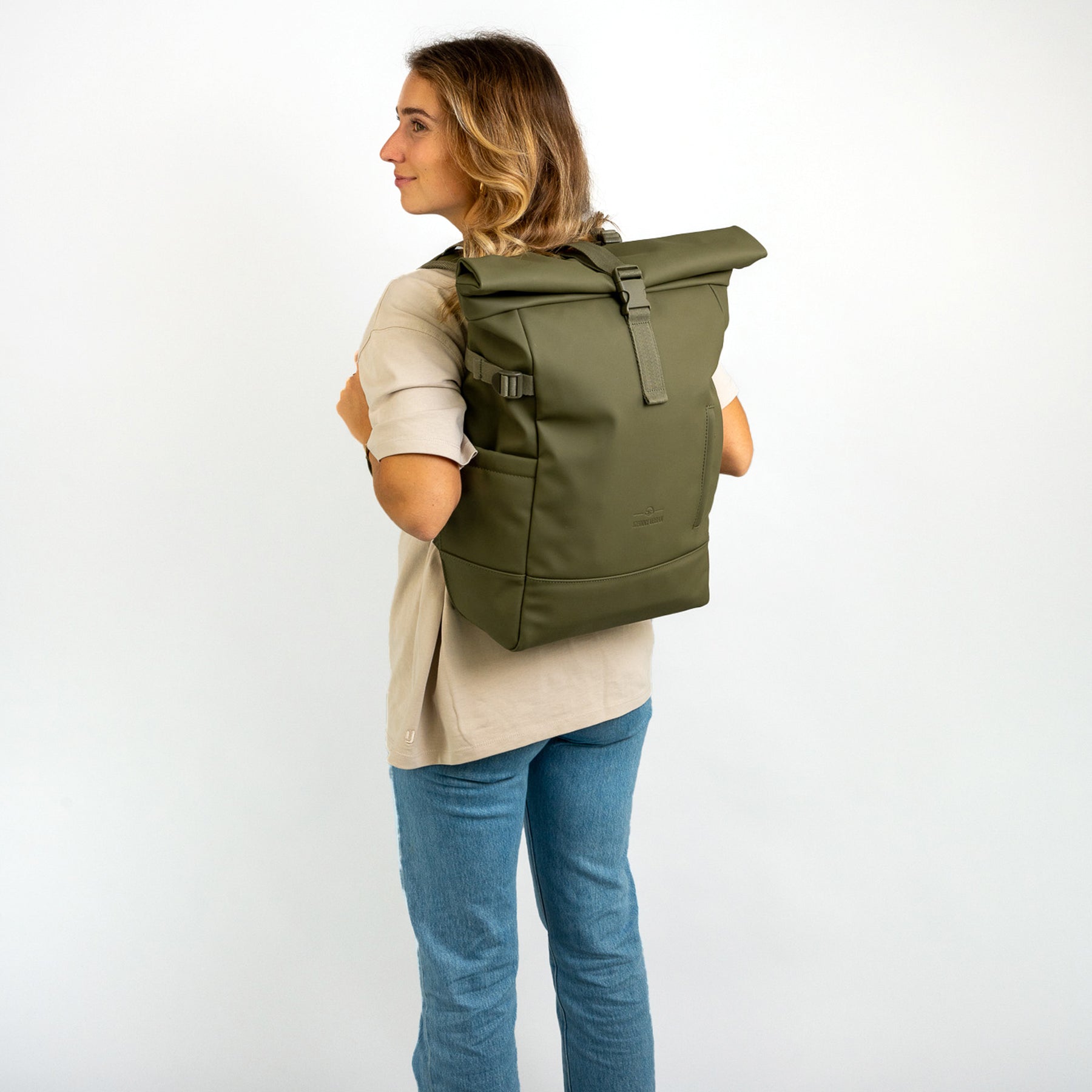 Frau mit olivgrünem Rolltop Rucksack 'Harvey Large' aus PU-Material, beige Shirt und blaue Jeans