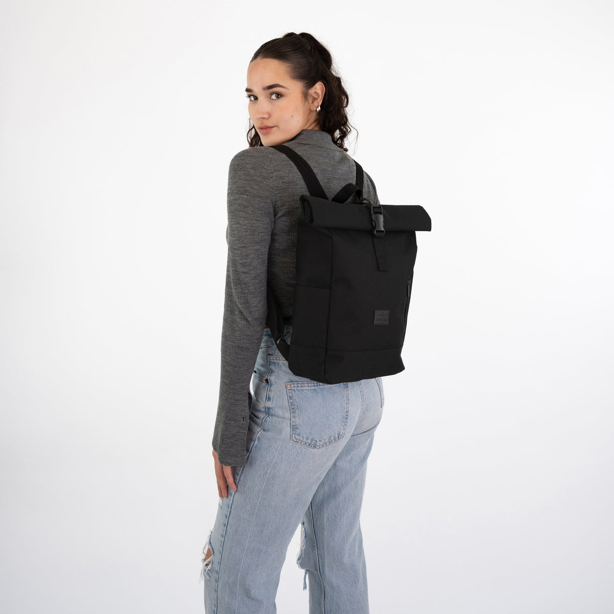 Frau mit grauem Langarmshirt und hellblauen Jeans trägt schwarzen Rolltop Rucksack 'Robin Small'