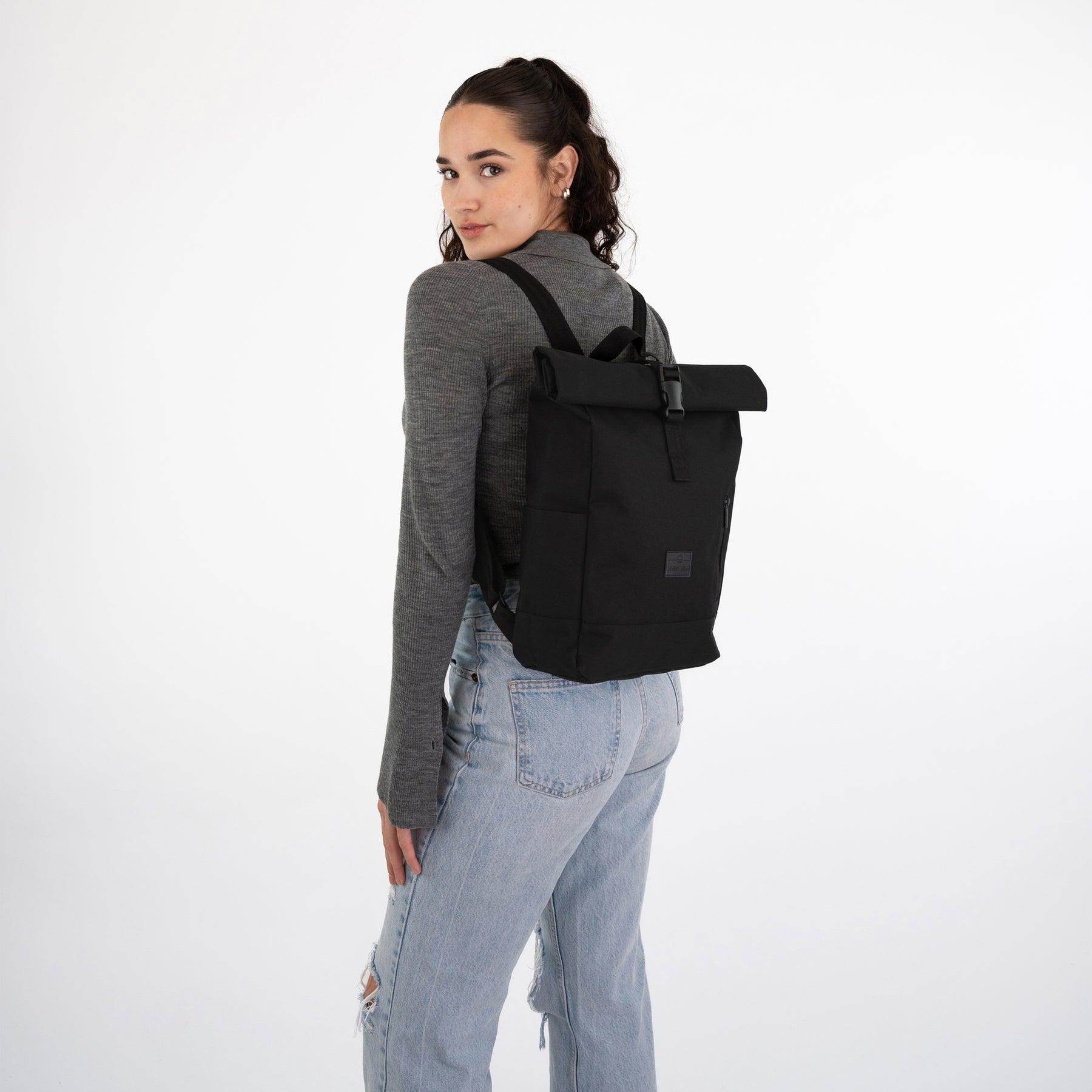 Frau mit grauem Langarmshirt und hellblauen Jeans trägt schwarzen Rolltop Rucksack 'Robin Small'