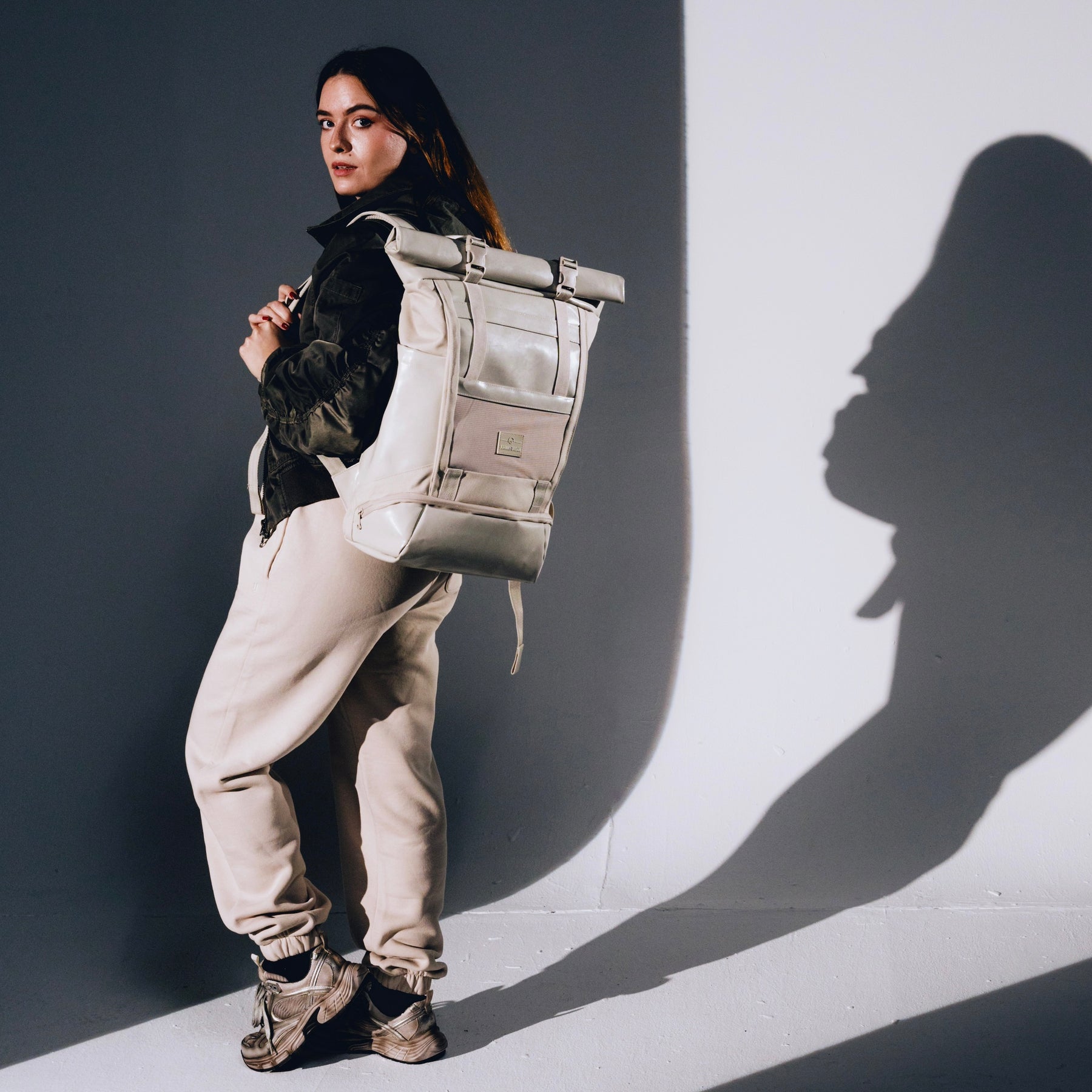Frau trägt beigen Rolltop Rucksack 'Ashton' mit schwarzer Jacke und beigen Jogginghosen