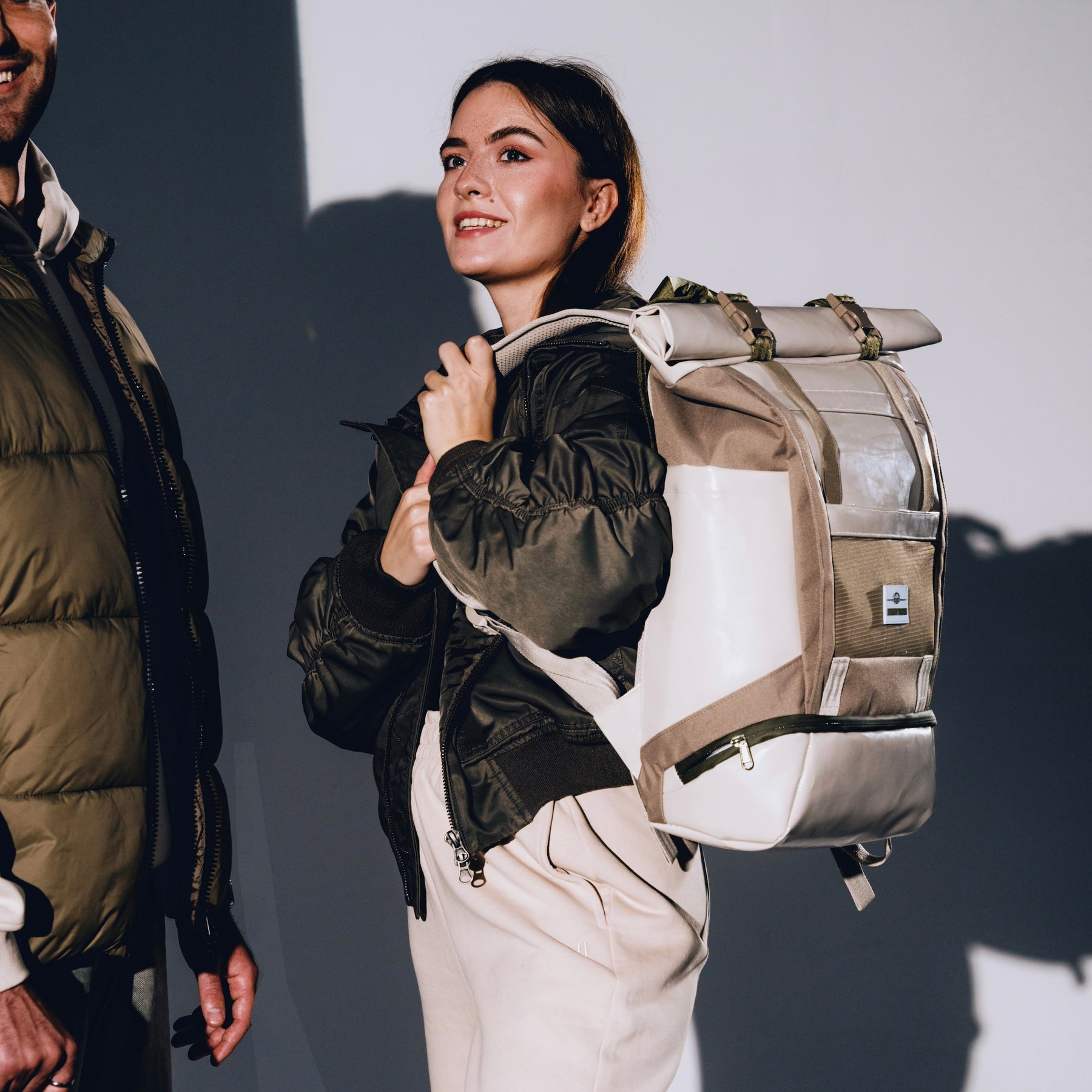 Frau trägt beigen Rolltop Rucksack 'Ashton' und schwarze Jacke