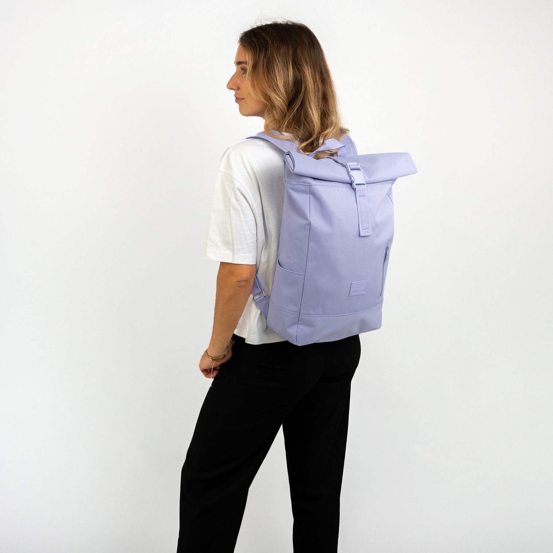 Frau mit helllila Rolltop Rucksack 'Robin Medium' von Johnny Urban, trägt weißes T-Shirt und schwarze Hose