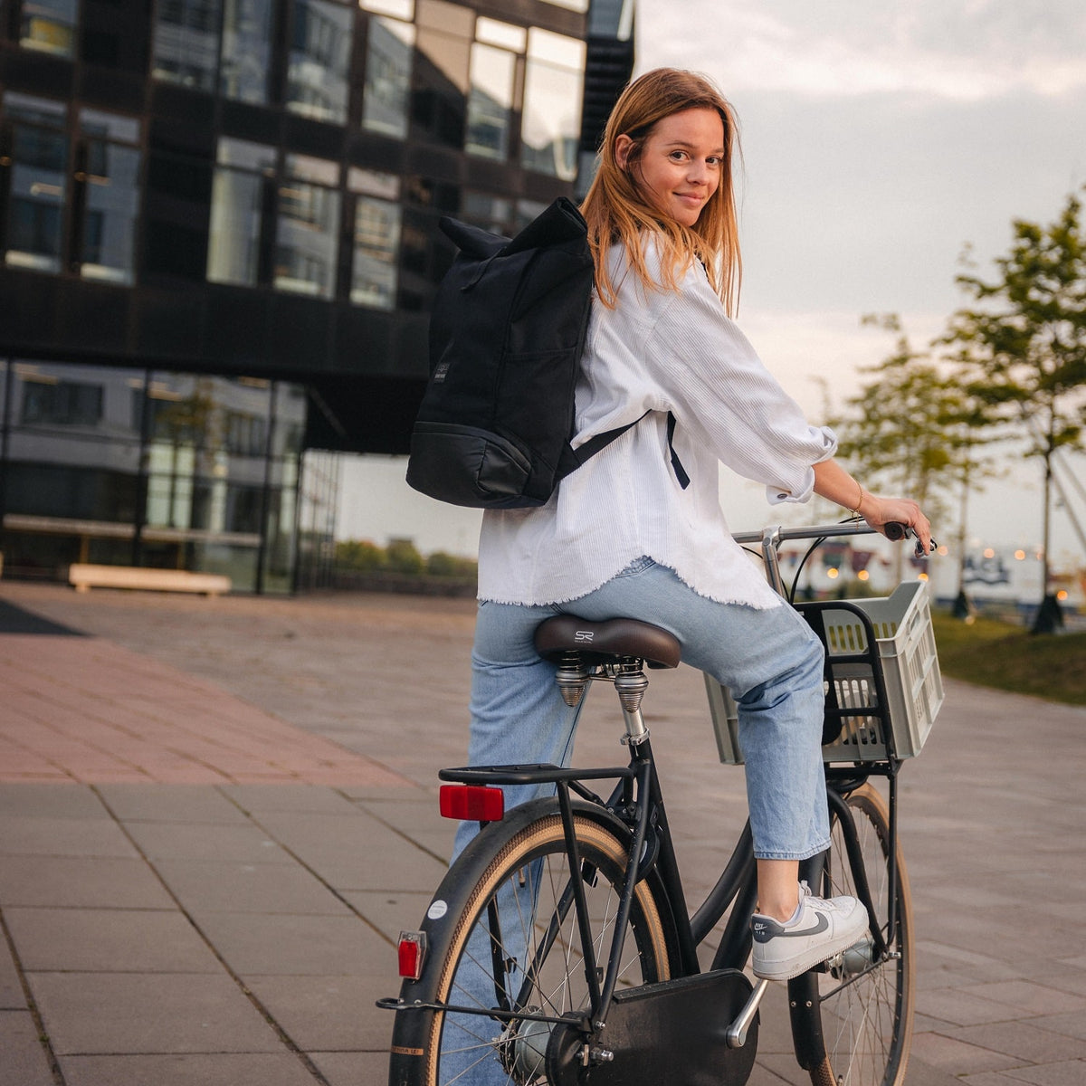 Frau auf Fahrrad trägt schwarzen Rolltop Rucksack Allen Medium von Johnny Urban