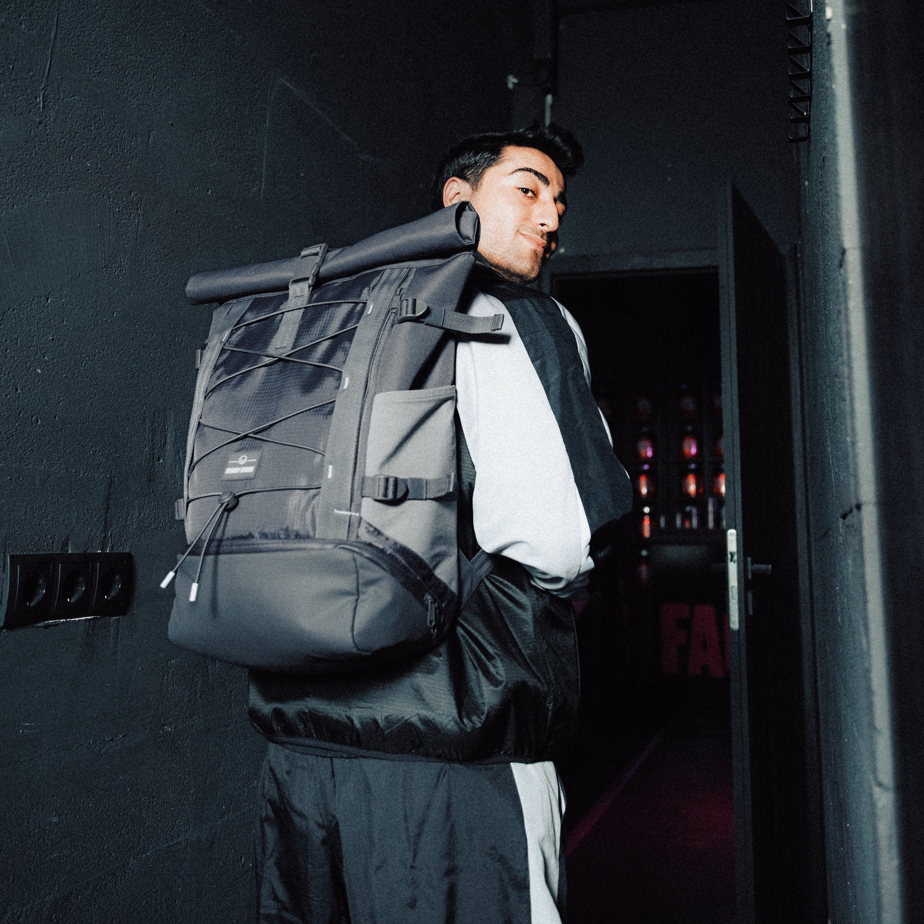 Mann trägt grauen Rolltop Rucksack 'Allen Large Move' von Johnny Urban in dunklem Flur