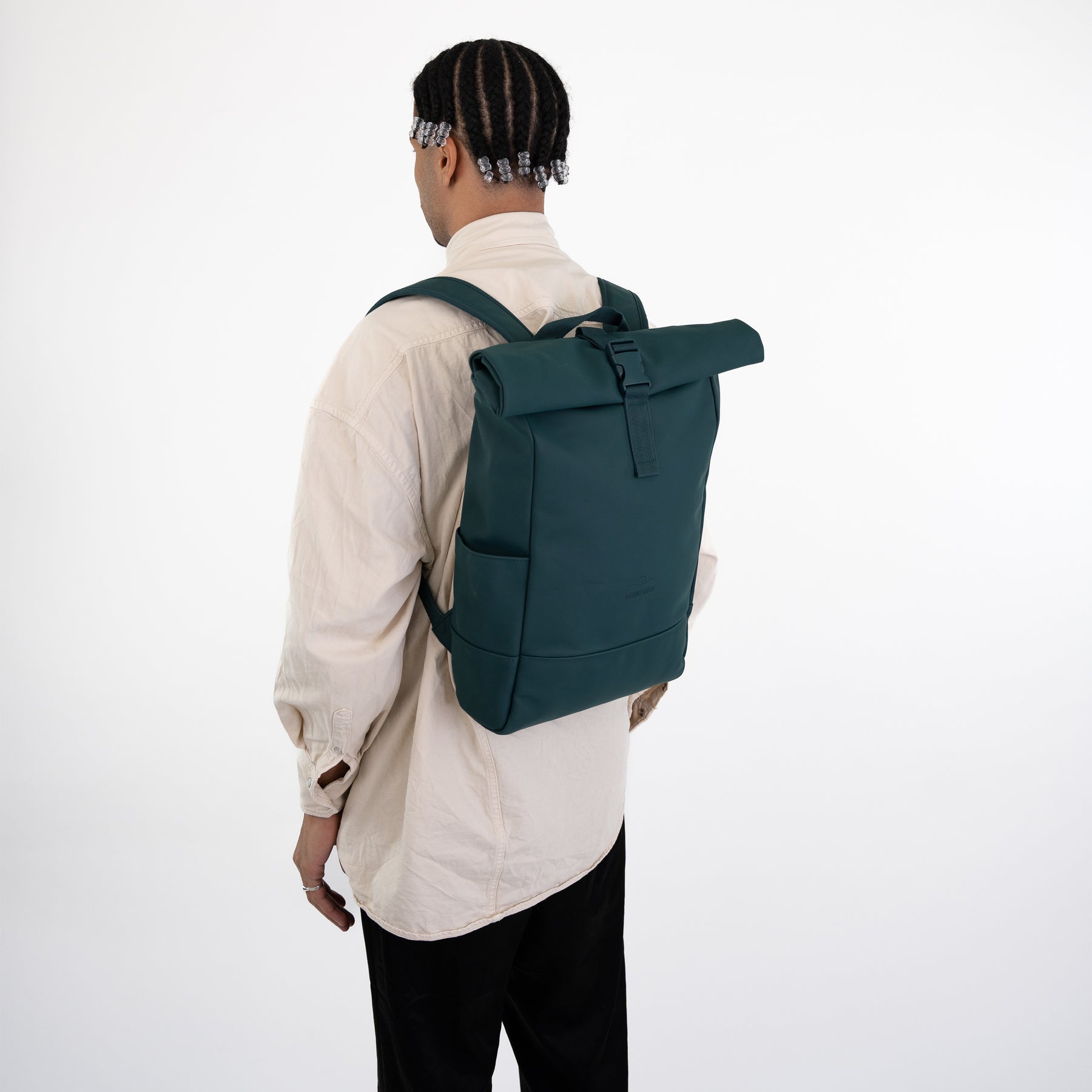 Mann trägt petrolfarbenen Rolltop Rucksack „Harvey Medium“ von Johnny Urban mit beige Hemd und schwarzer Hose