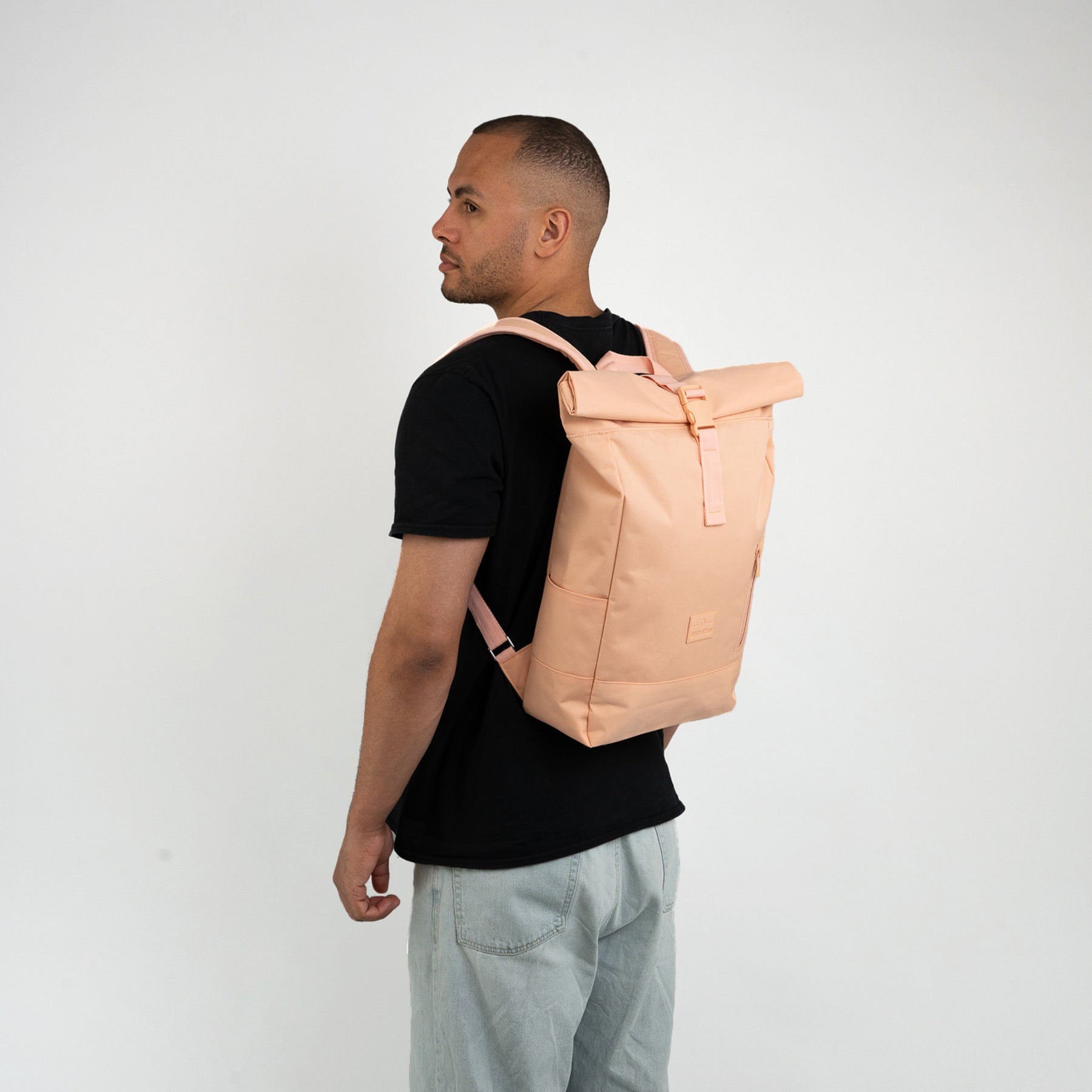 Mann von der Seite mit Johnny Urban Rolltop Rucksack 'Robin Medium' in Rosa und schwarzem T-Shirt