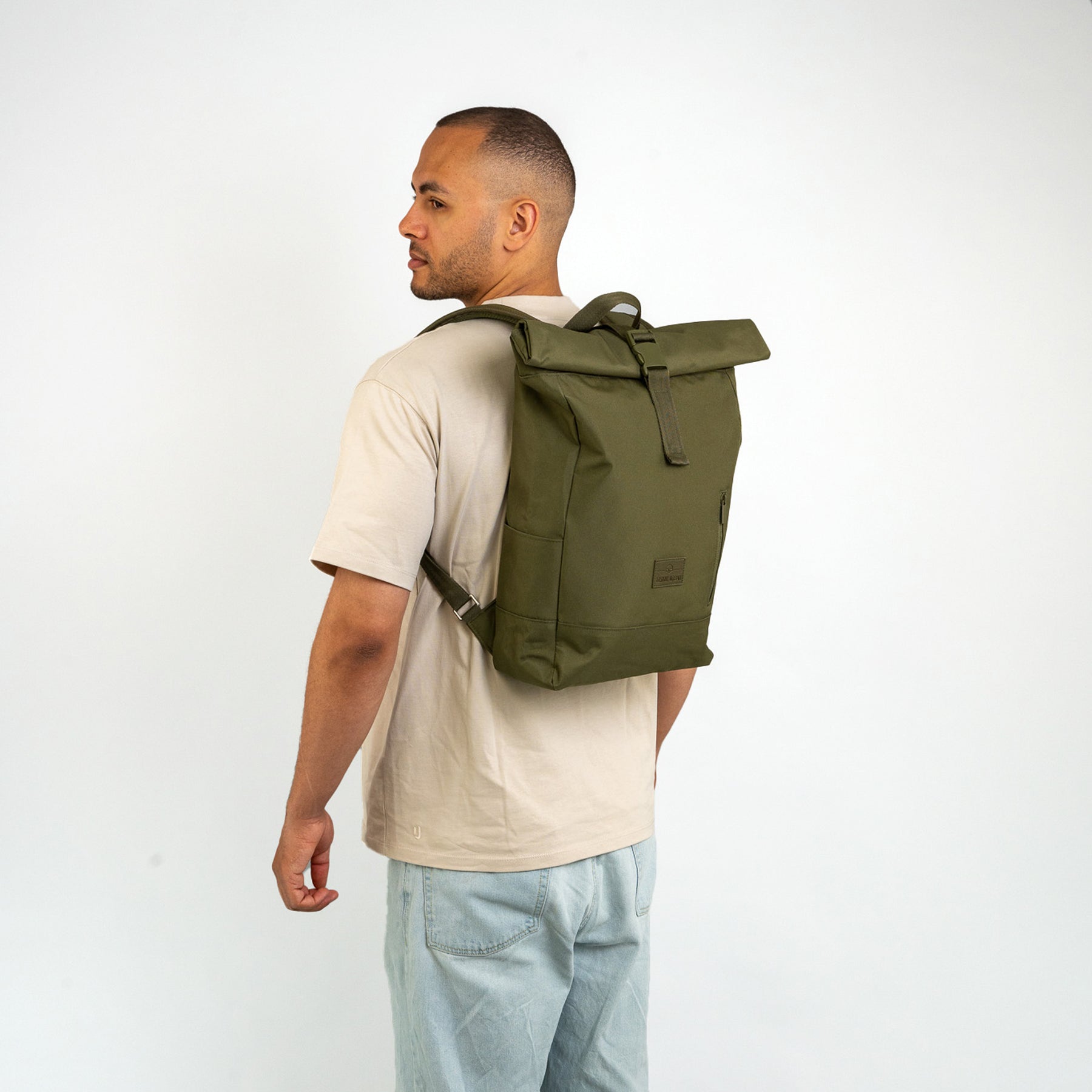 Mann trägt olivegrünen Rolltop-Rucksack 'Robin Medium' von Johnny Urban, trägt helles T-Shirt und Jeans