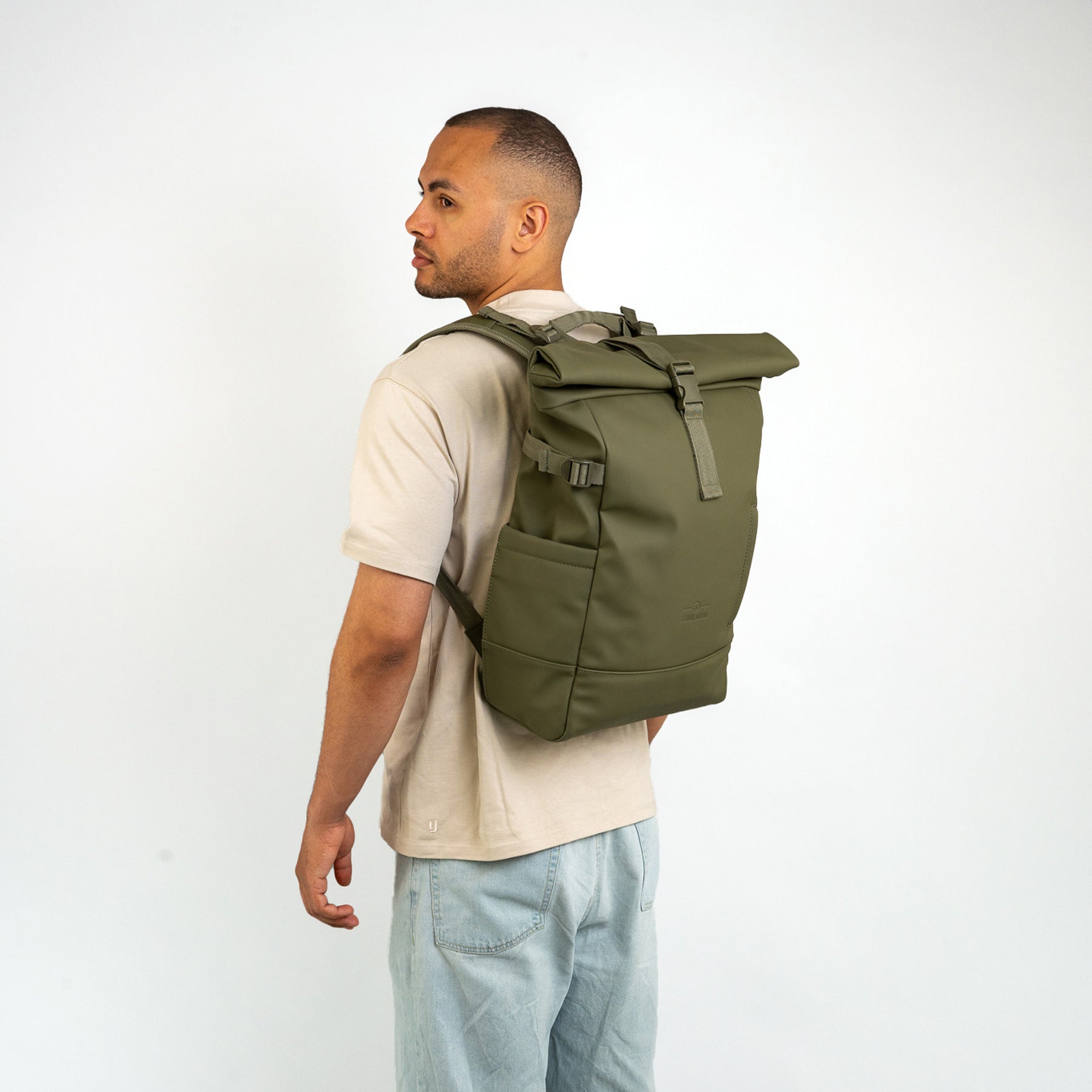 Mann trägt olivgrünen Rolltop Rucksack 'Harvey Large' von Johnny Urban, beige T-Shirt, helle Jeans