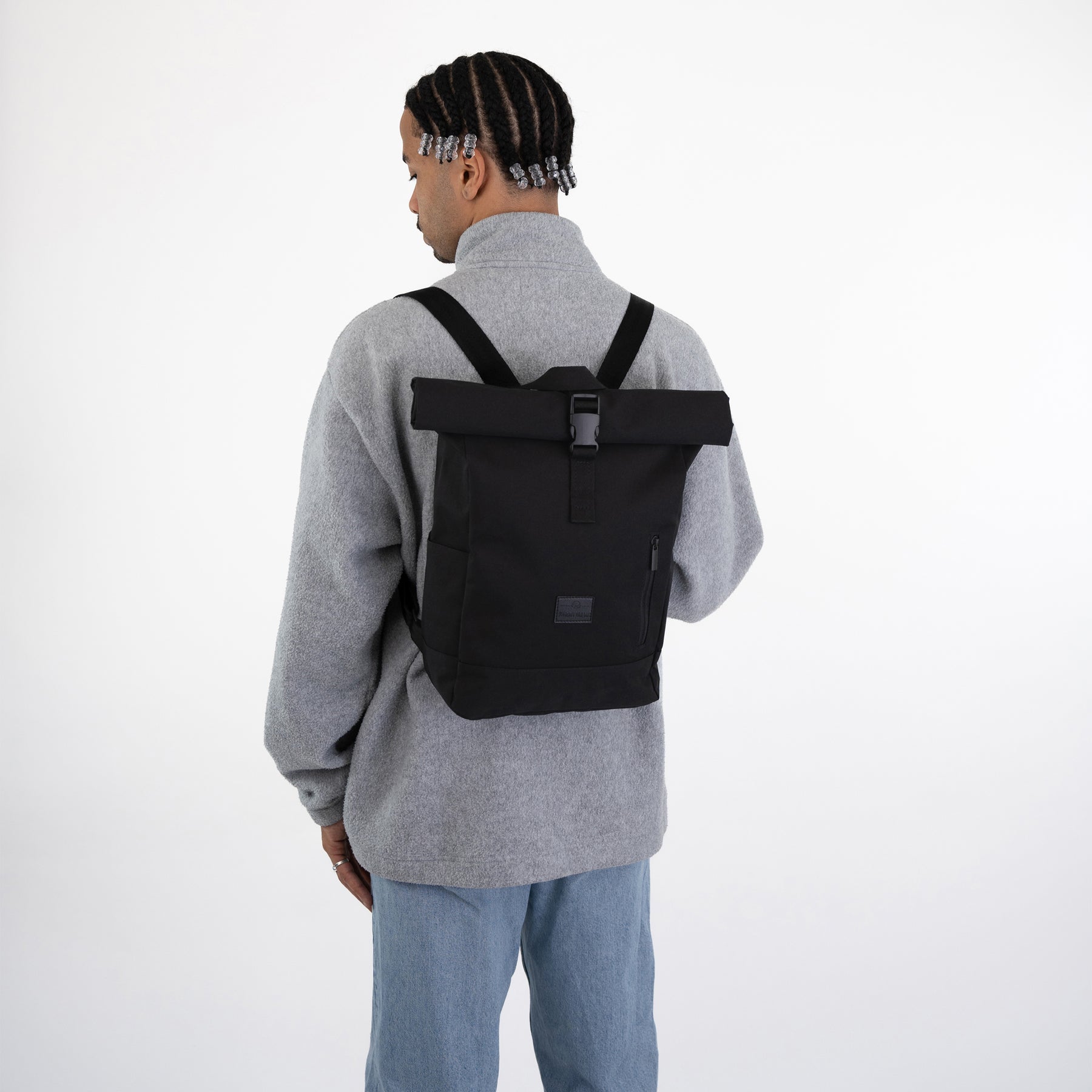 Schwarzer Rolltop Rucksack 'Robin Small' auf dem Rücken eines Mannes mit grauem Pullover und blauer Jeans