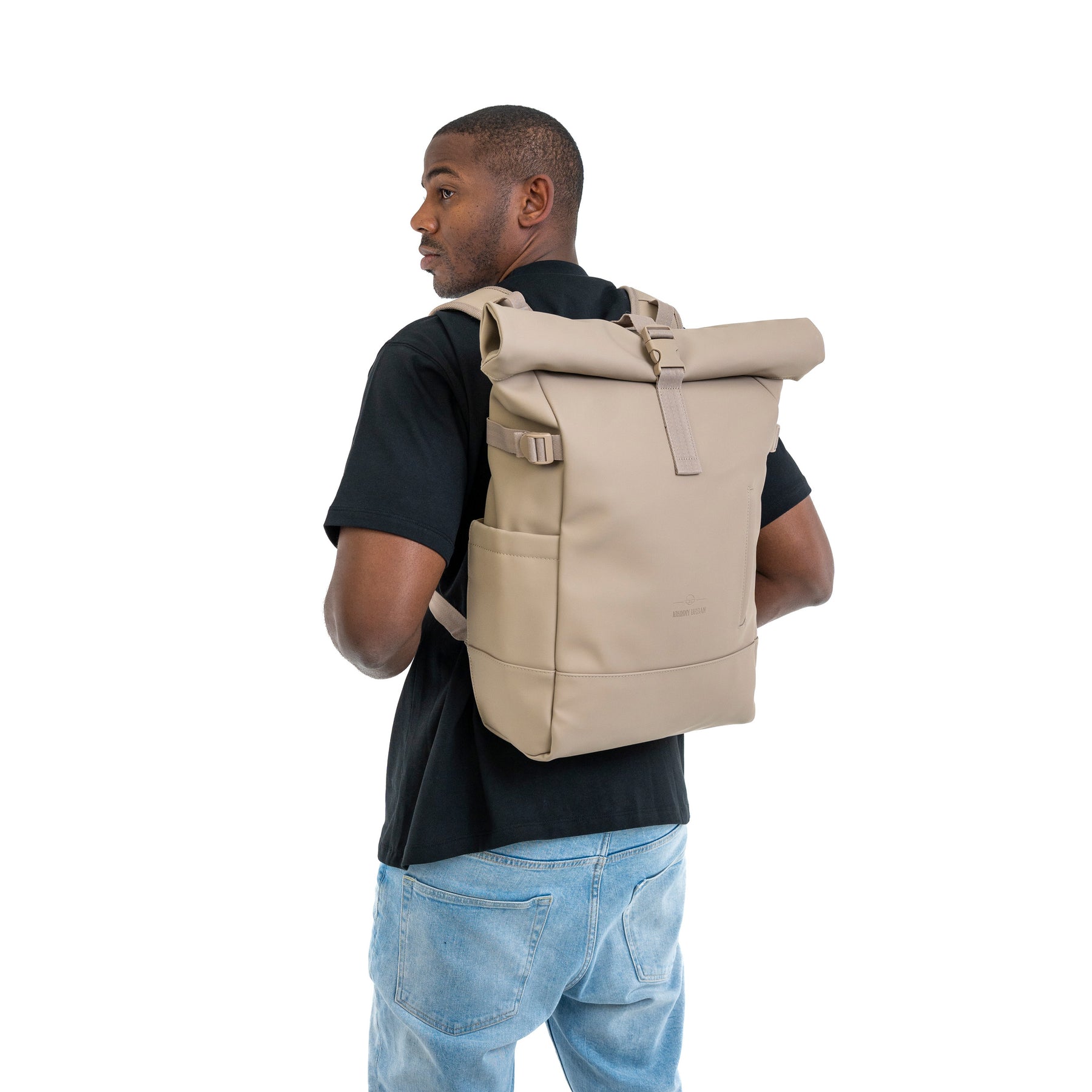 Beiger Rolltop-Rucksack 'Harvey Large' von Johnny Urban auf dem Rücken eines Mannes mit schwarzem T-Shirt und blauer Jeans