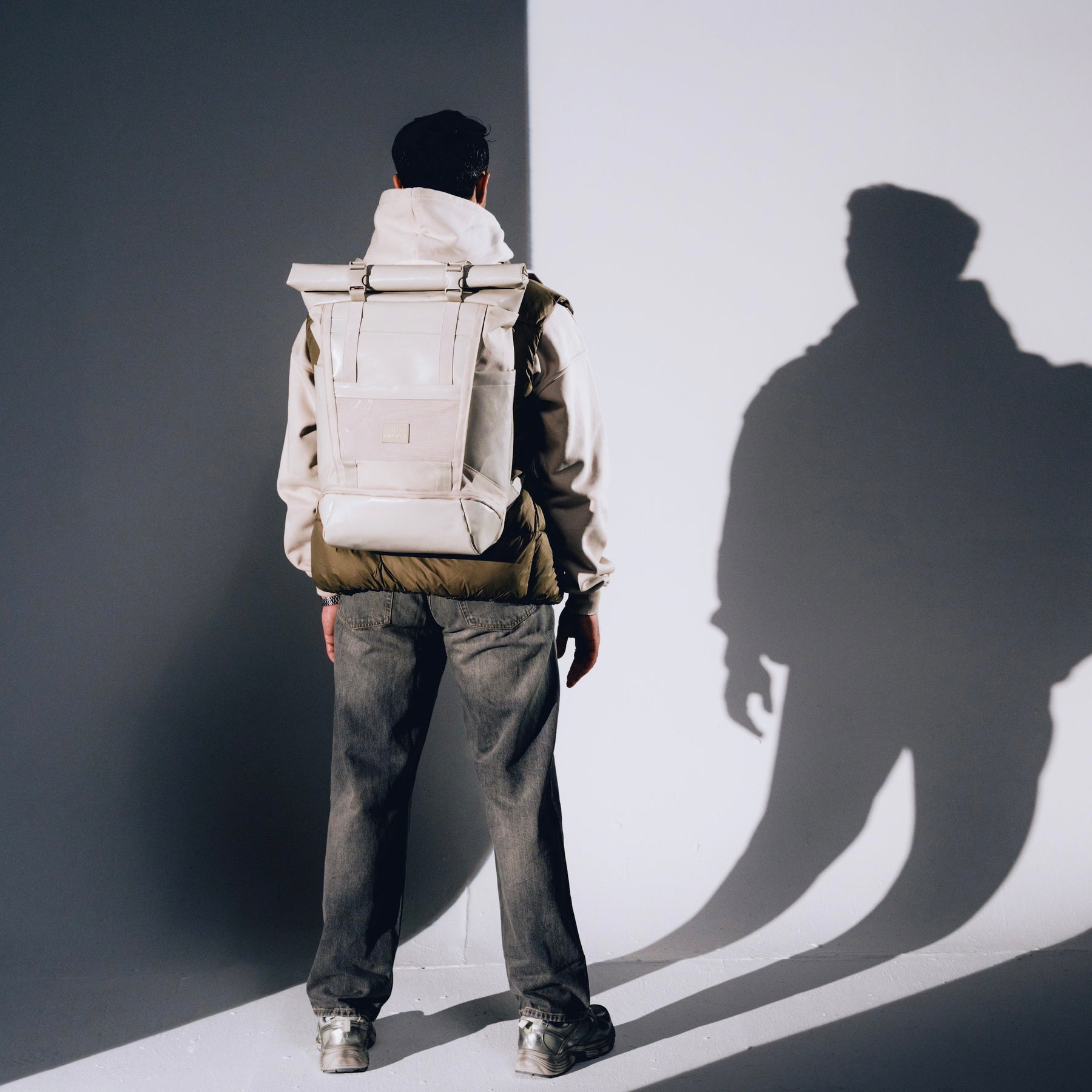 Mann von hinten mit beigefarbenem Rolltop-Rucksack 'Ashton' von Johnny Urban, trägt grüne Weste und graue Jeans