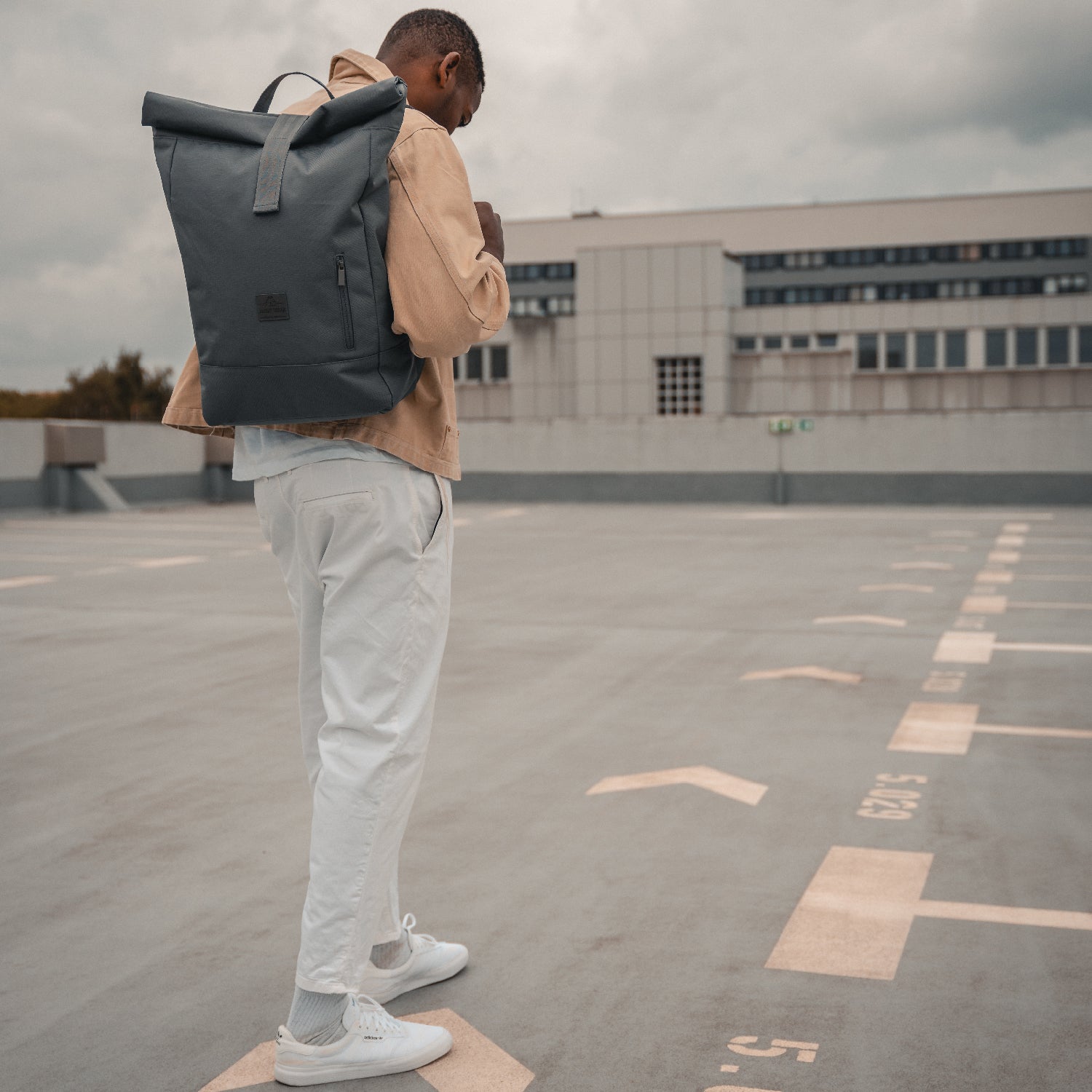Mann von hinten mit dunkelgrauem Rolltop Rucksack ‚Robin Large‘ von Johnny Urban auf einem Parkdeck