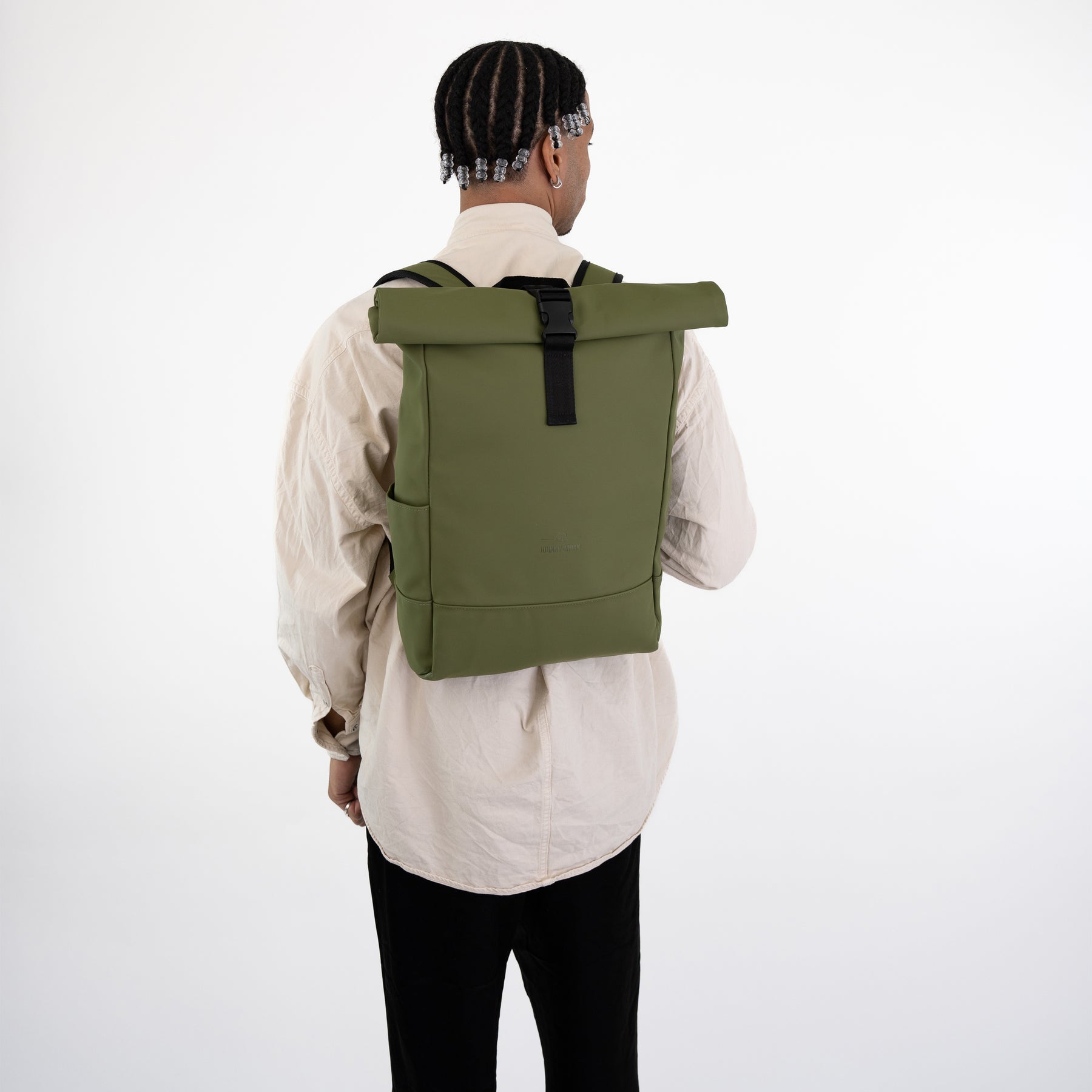 Mann trägt grünen Rolltop Rucksack 'Harvey Medium' mit schwarzem Verschluss, beige Hemd und schwarze Hose