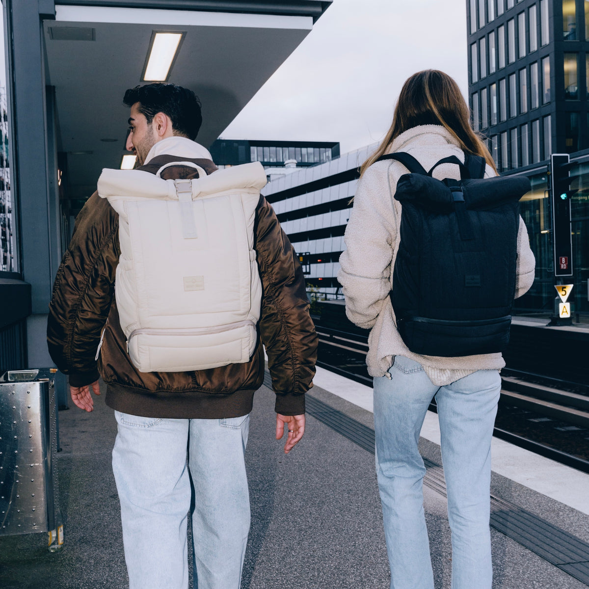 Zwei Personen in urbaner Umgebung tragen Rolltop-Rucksäcke 'Kyle' von Johnny Urban, einer hellbeige, der andere schwarz