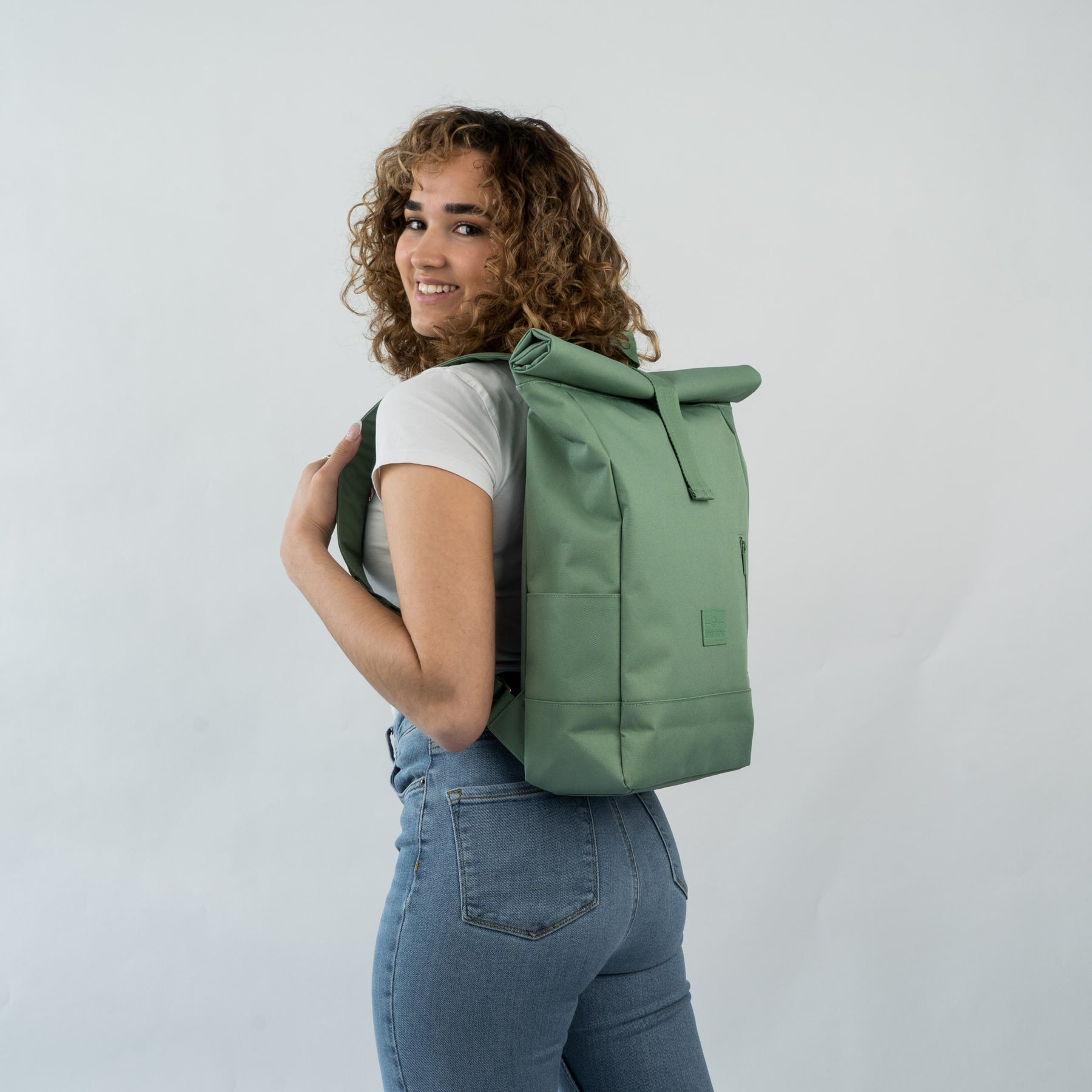 Frau trägt grünen Rolltop-Rucksack 'Robin Medium' von Johnny Urban, weißes T-Shirt, blaue Jeans