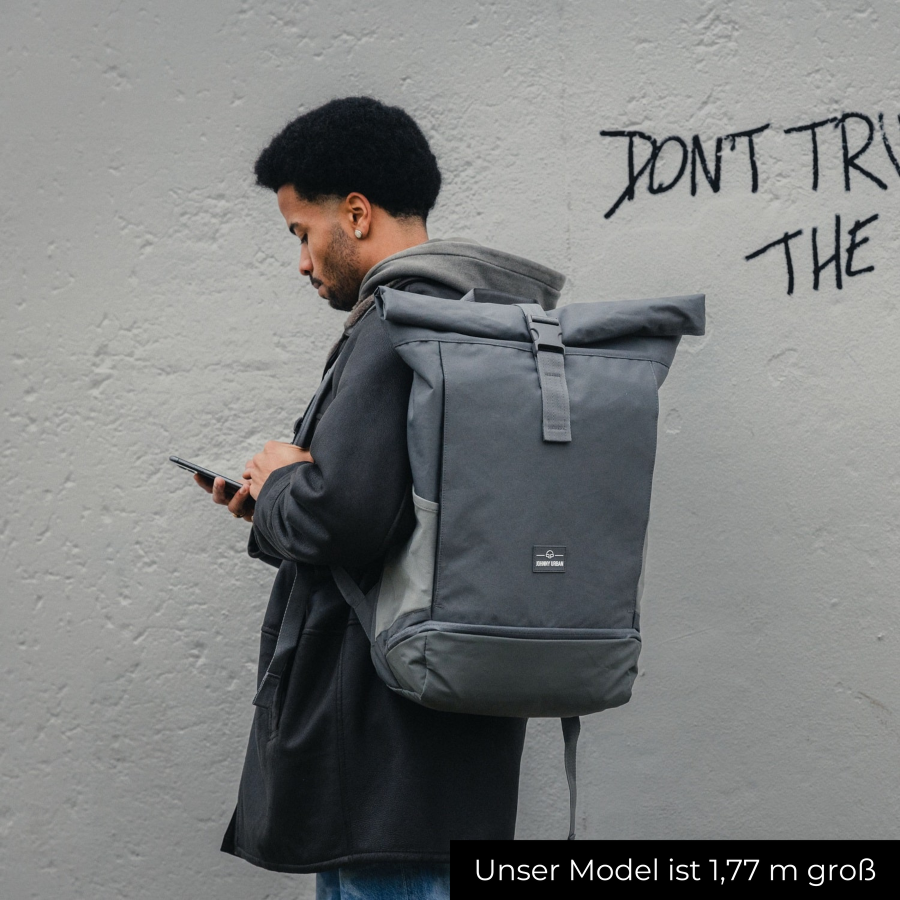 Mann mit 1,77 m Größe trägt grauen Rolltop Rucksack 'Allen XL' von Johnny Urban und schaut auf sein Handy