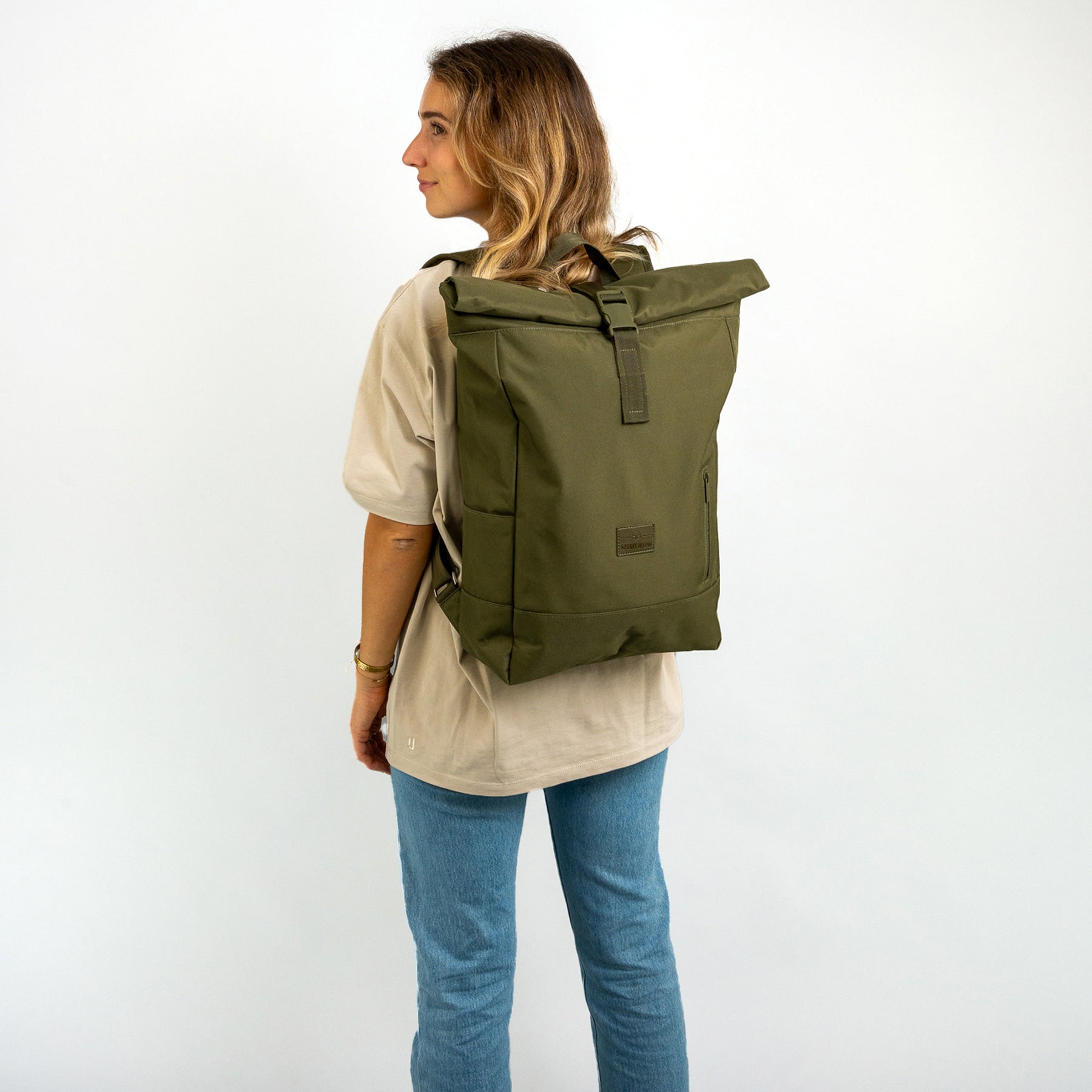 Frau trägt olivefarbenen Rolltop-Rucksack 'Robin Large' über einem beigen T-Shirt und blauen Jeans