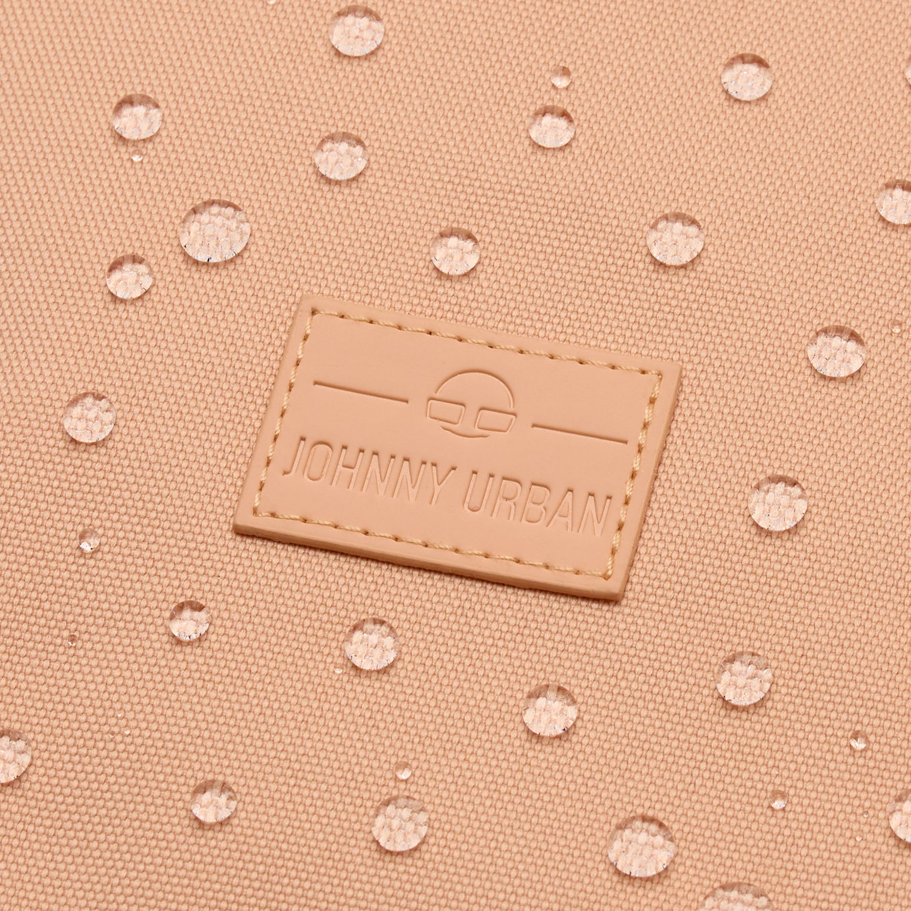 Nahaufnahme eines pfirsichfarbenen Johnny Urban Rolltop-Rucksacks 'Robin Small' mit wasserabweisender Oberfläche und Wassertropfen