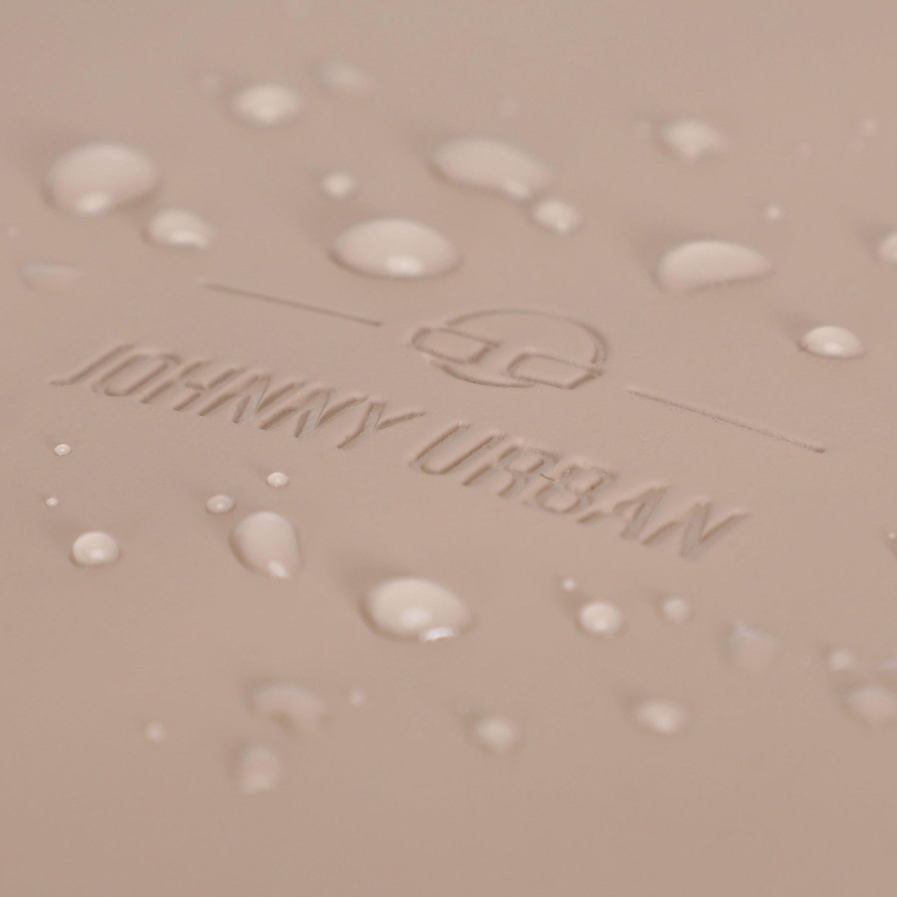Nahe Aufnahme des beigen wasserdichten Materials mit dem eingeprägten Johnny Urban Logo und Wassertropfen