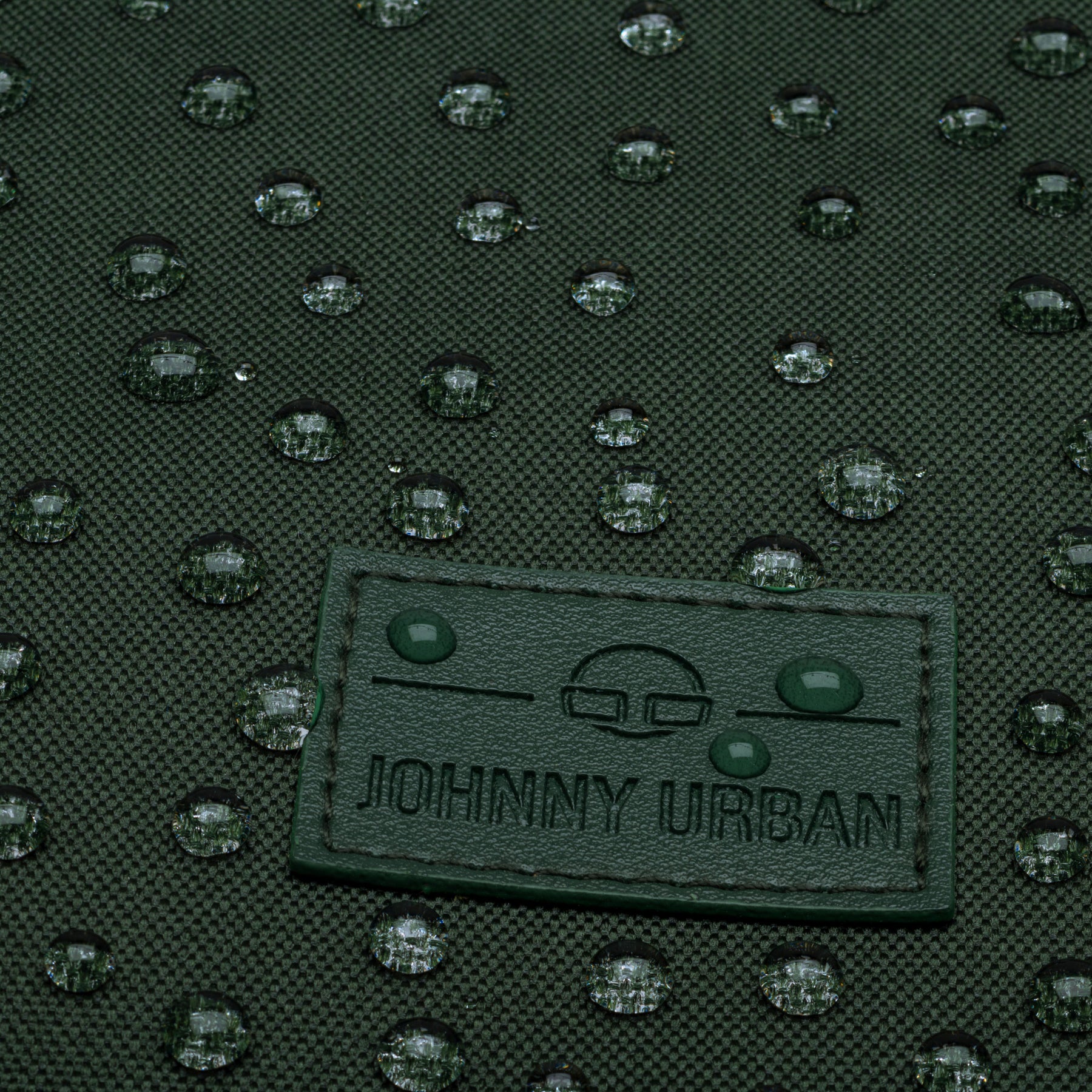 Nahaufnahme des wasserabweisenden grünen Rolltop-Rucksacks 'Robin Medium' von Johnny Urban mit Tropfen auf dem Stoff
