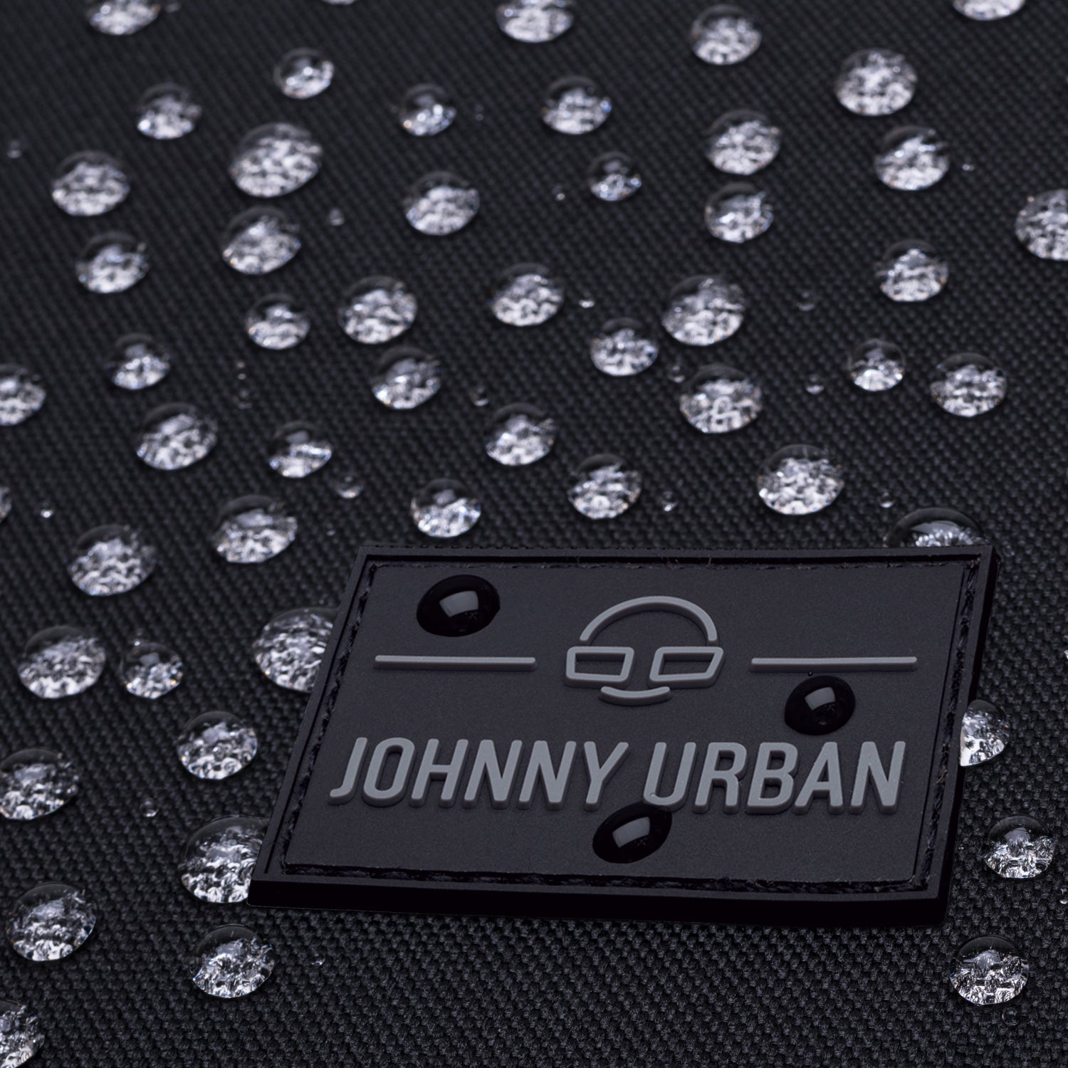 Nahaufnahme des Johnny Urban Logos auf dem wasserdichten Rolltop Rucksack Allen Large mit Wassertropfen