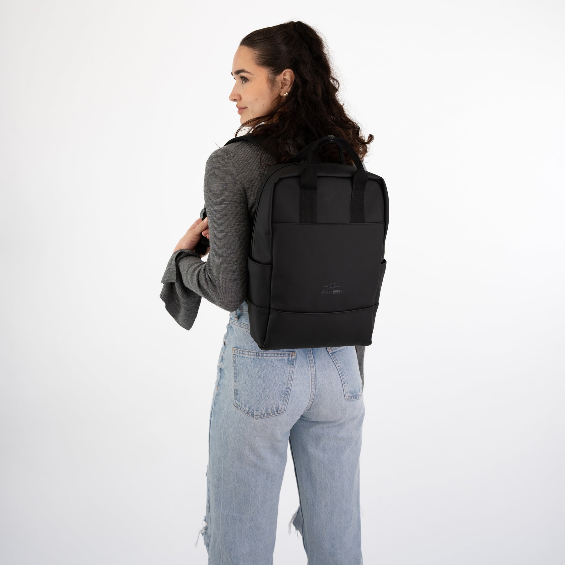 Frau mit schwarzen Rucksack 'Hailey' trägt grauen Pullover und hellblaue Jeans