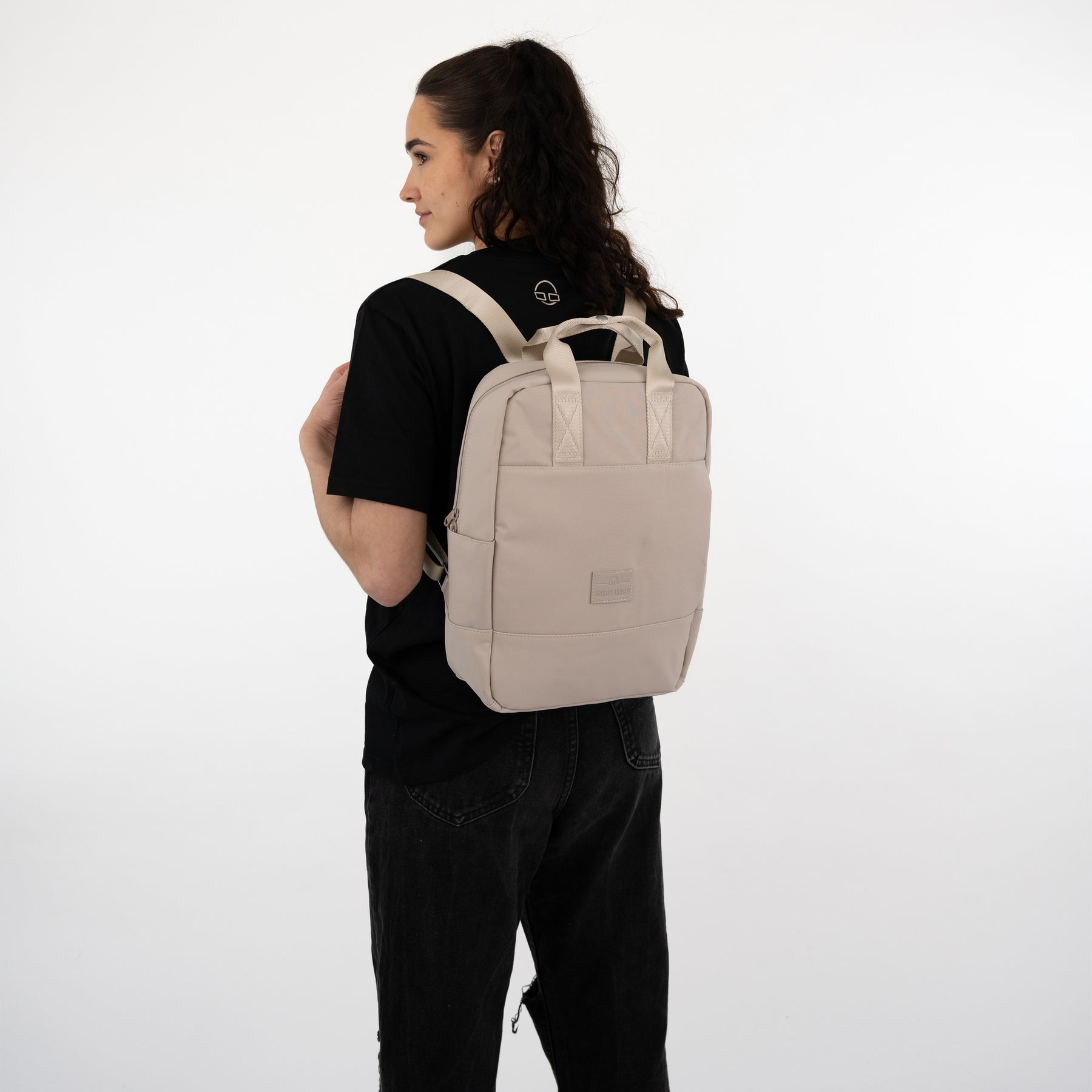 Frau mit beigem Johnny Urban Rucksack 'Jona Medium' und schwarzem T-Shirt und Hose