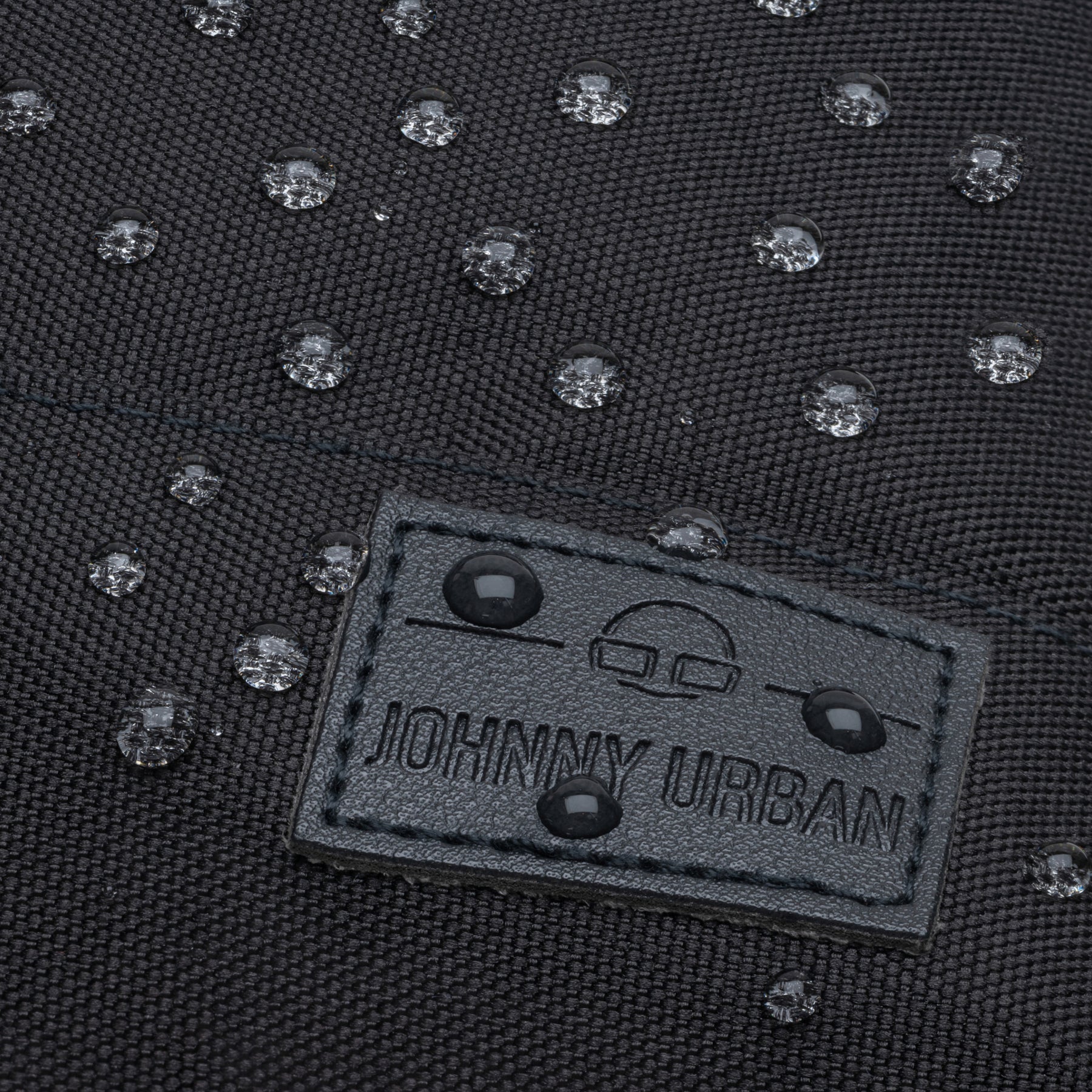 Nahaufnahme von wasserdichten Regentropfen auf dem schwarzen Stoff des Damenrucksacks 'Mia' von Johnny Urban