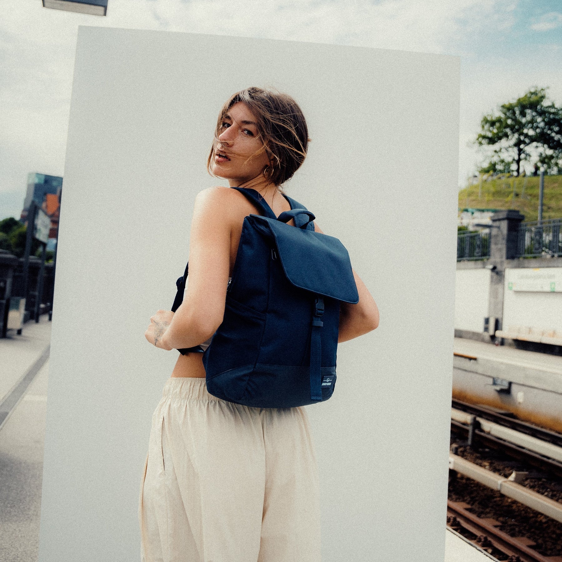 Frau mit glattem dunkelblauem Johnny Urban Rucksack 'Mika' vor weißem Hintergrund und Bahngleisen