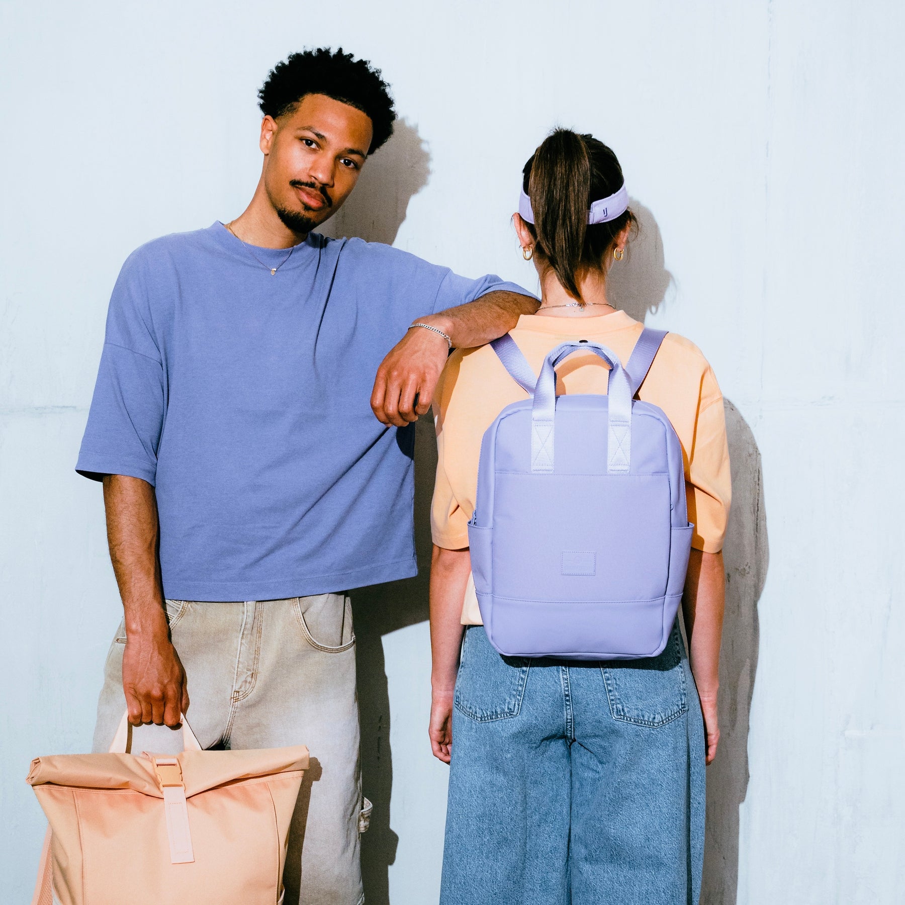 Frau trägt lila Rucksack 'Jona Medium', Mann steht neben ihr mit beiger Tasche in der Hand