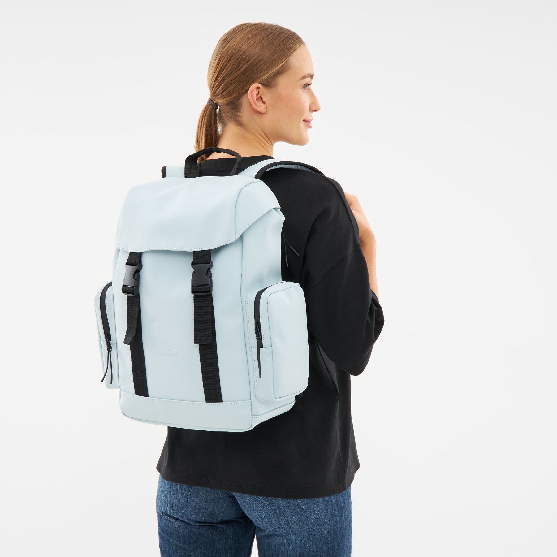 Frau mit hellblauem 'Finley' Rucksack von Johnny Urban, schwarzes Oberteil, blaue Jeans