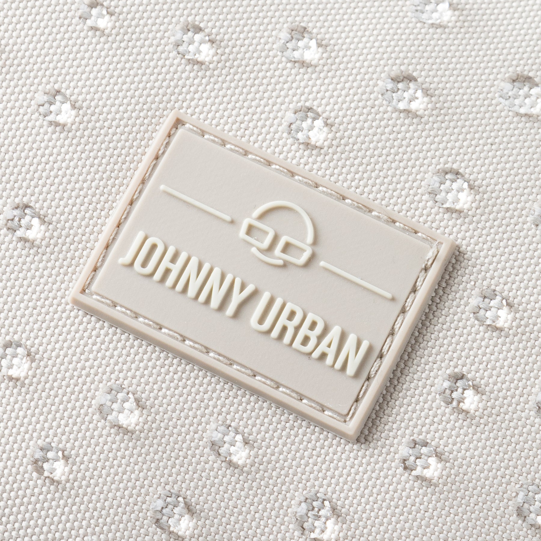Nahaufnahme des Johnny Urban Logos auf sandfarbenem, wasserdichtem Rucksackstoff mit gepunkteter Struktur