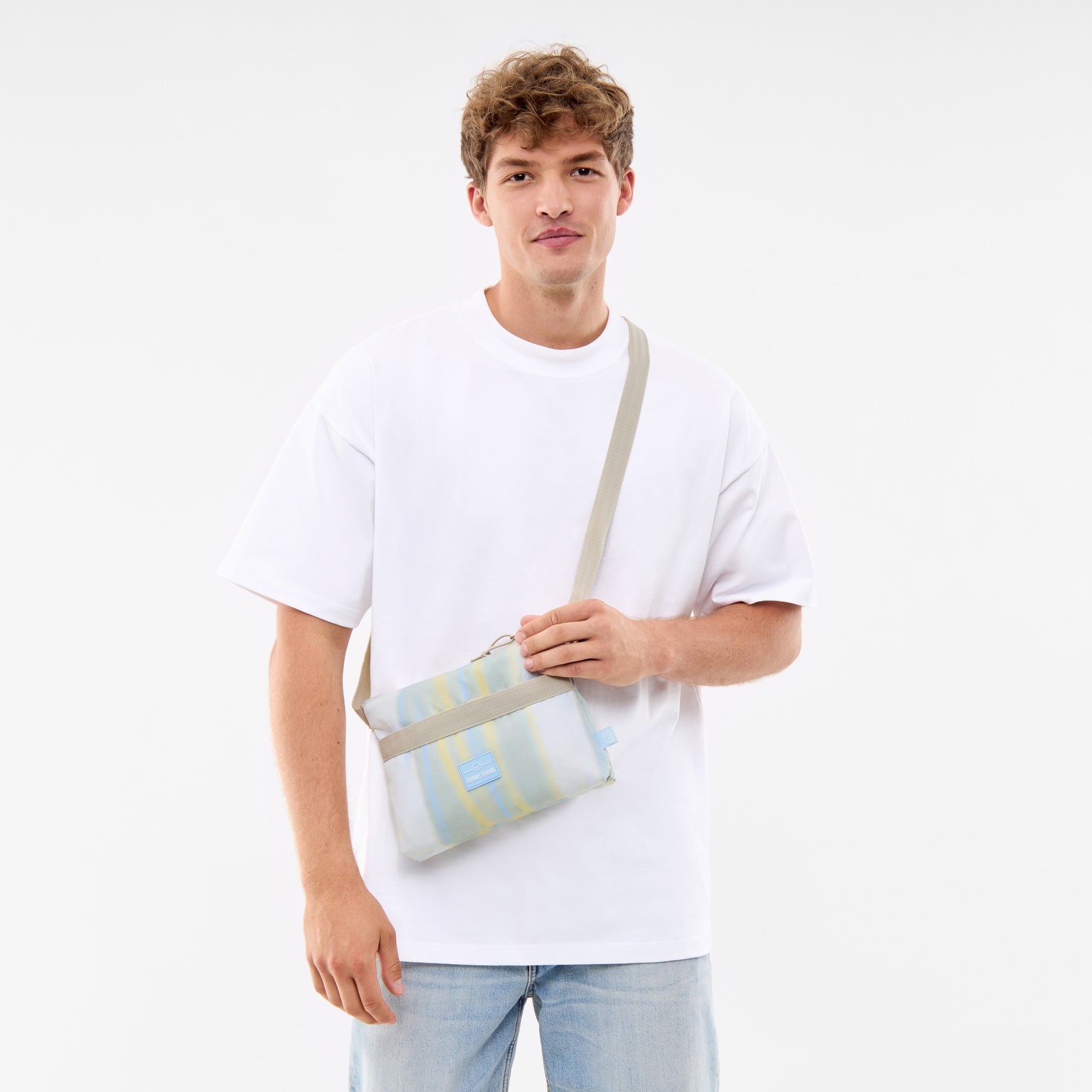 Mann trägt die bunte Umhängetasche 'Drew' mit verstellbarem Trageriemen über weißem T-Shirt