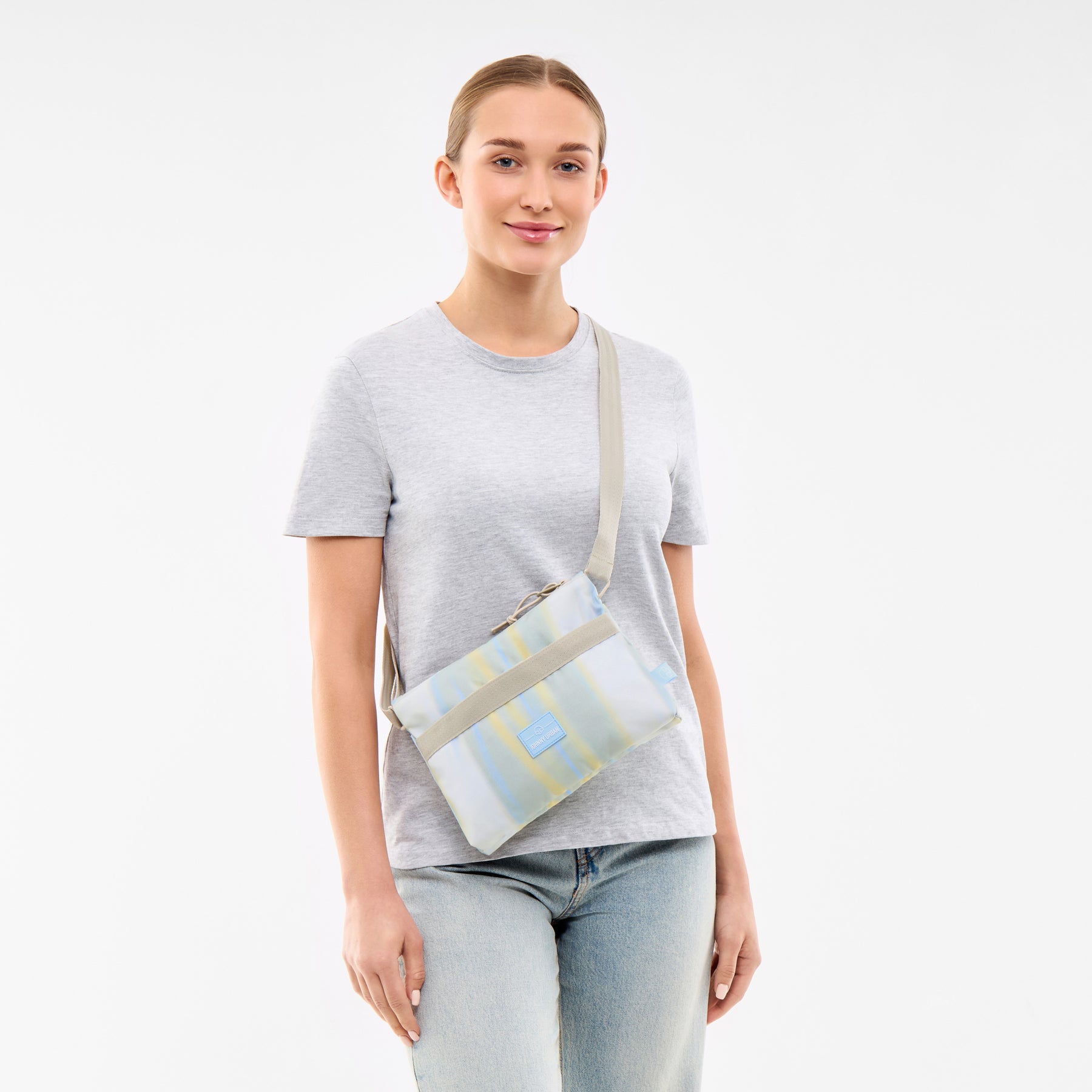 Frau trägt helle Umhängetasche 'Drew' mit pastellfarbenen Streifen und verstellbarem Gurt