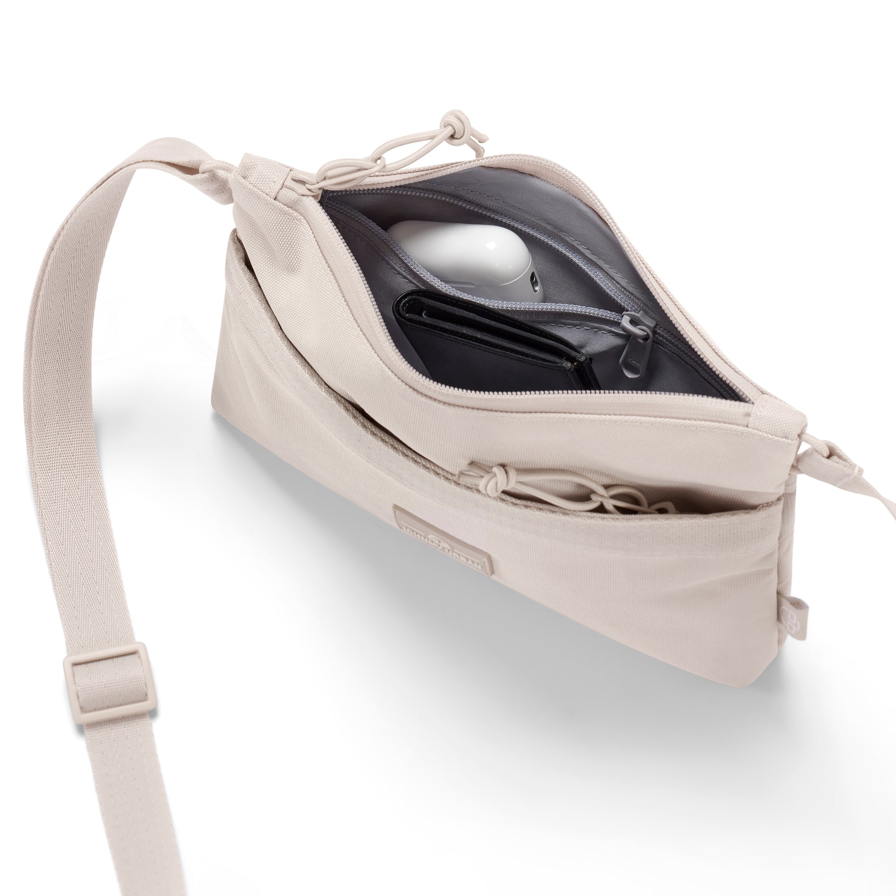 Umhängetasche 'Drew' in Sandfarbe mit offenem Hauptfach, darin schwarze Geldbörse und weißes Ladegerät