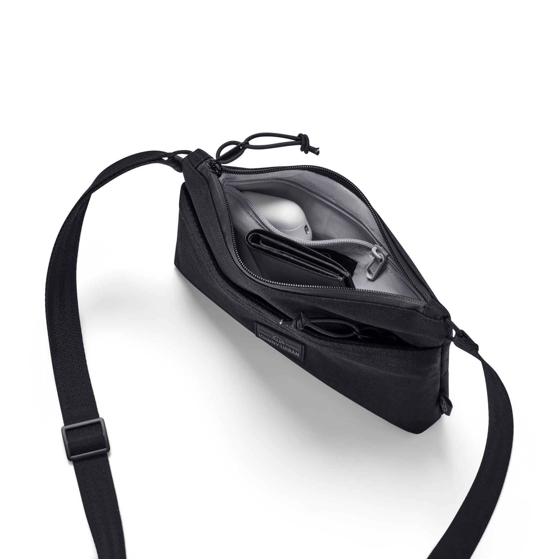 Schwarze Umhängetasche 'Drew' von Johnny Urban geöffnet mit sichtbarem Innenfach, das einen silbernen Gegenstand und eine schwarze Geldbörse enthält
