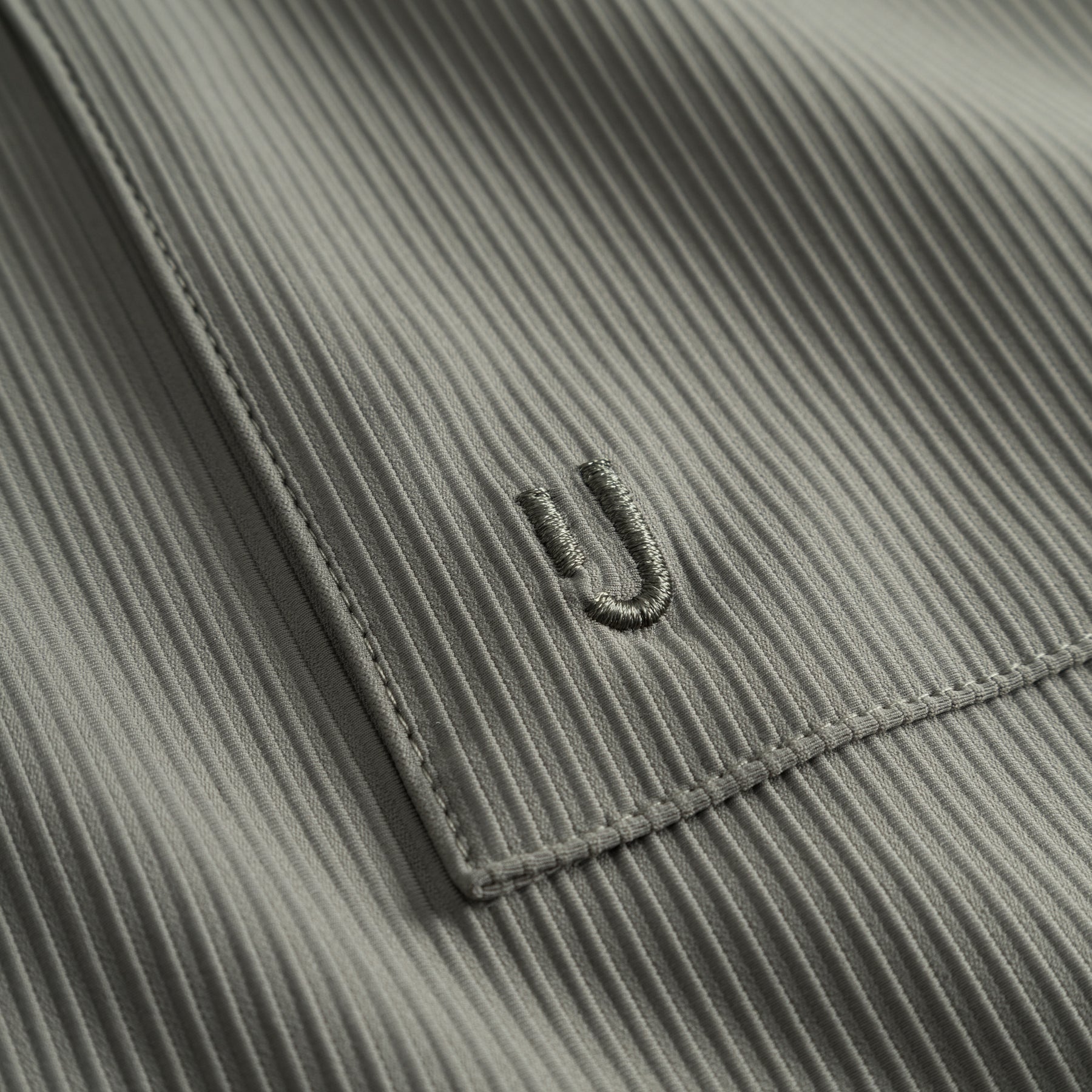 Naheinstellung eines olivgrauen, gerippten Stoffabschnitts mit einem gestickten 'ü'
