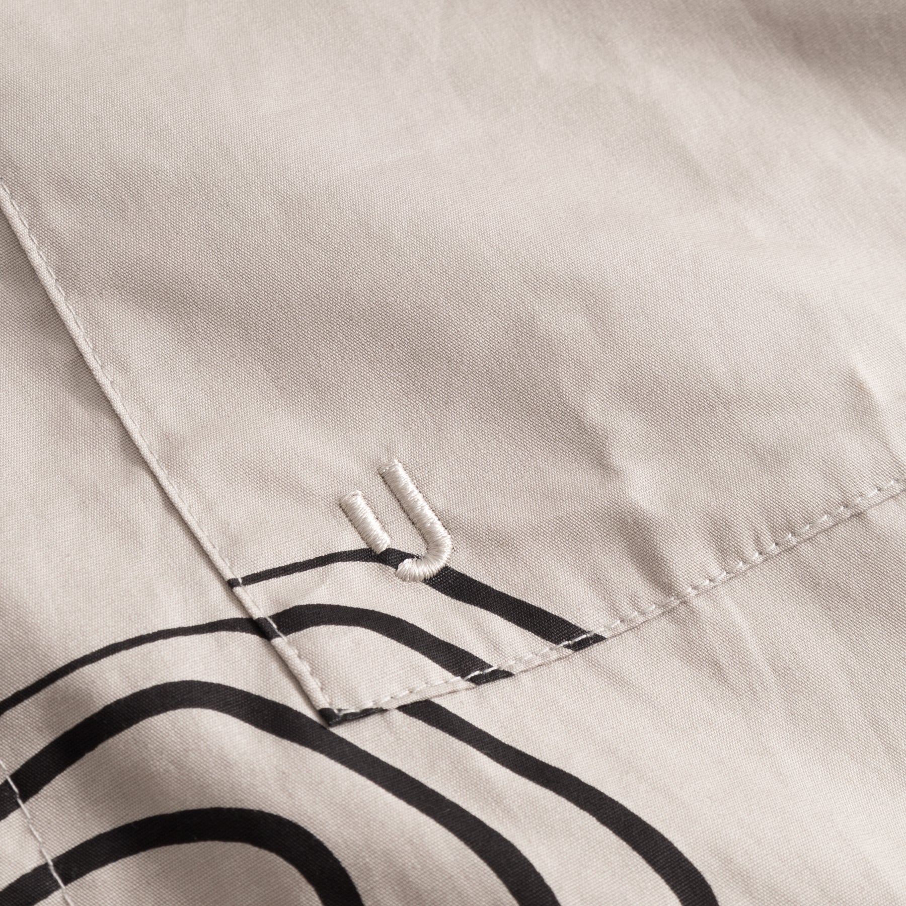 Sandfarbene Baumwolltasche mit schwarzem, abstraktem Linienmuster und gesticktem 'JU'-Logo