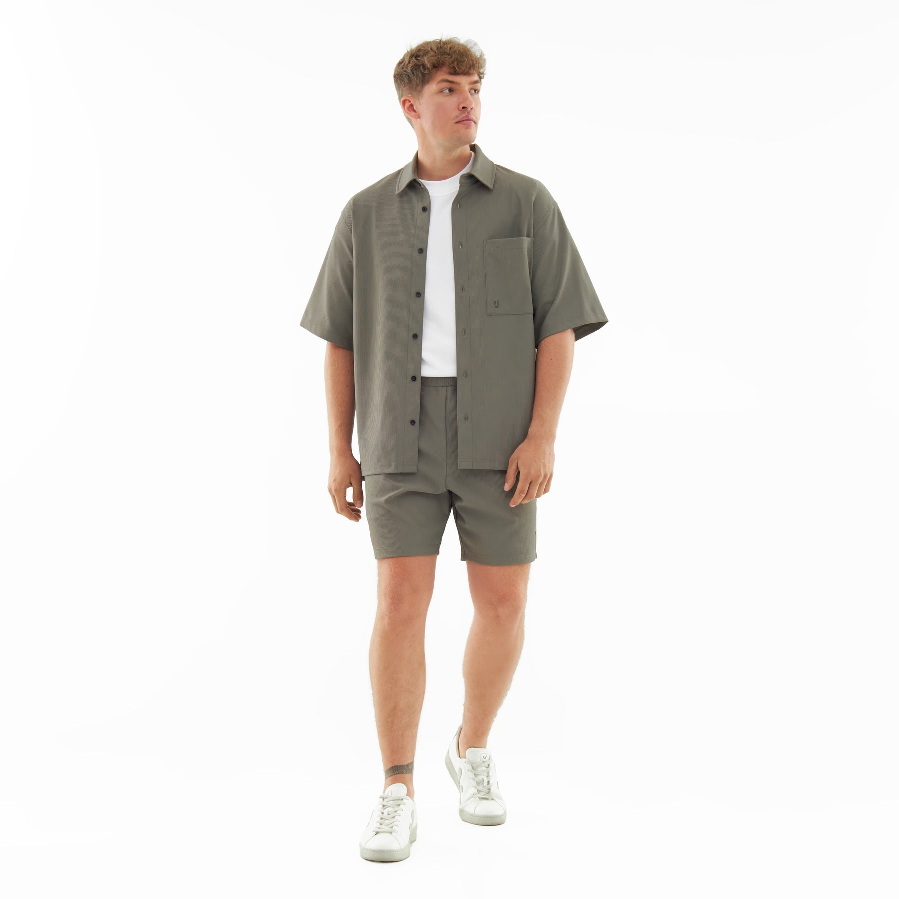 Männliches Model trägt olivegrüne Shorts 'Mason' und passende Hemdjacke mit weißem T-Shirt und weißen Sneakers