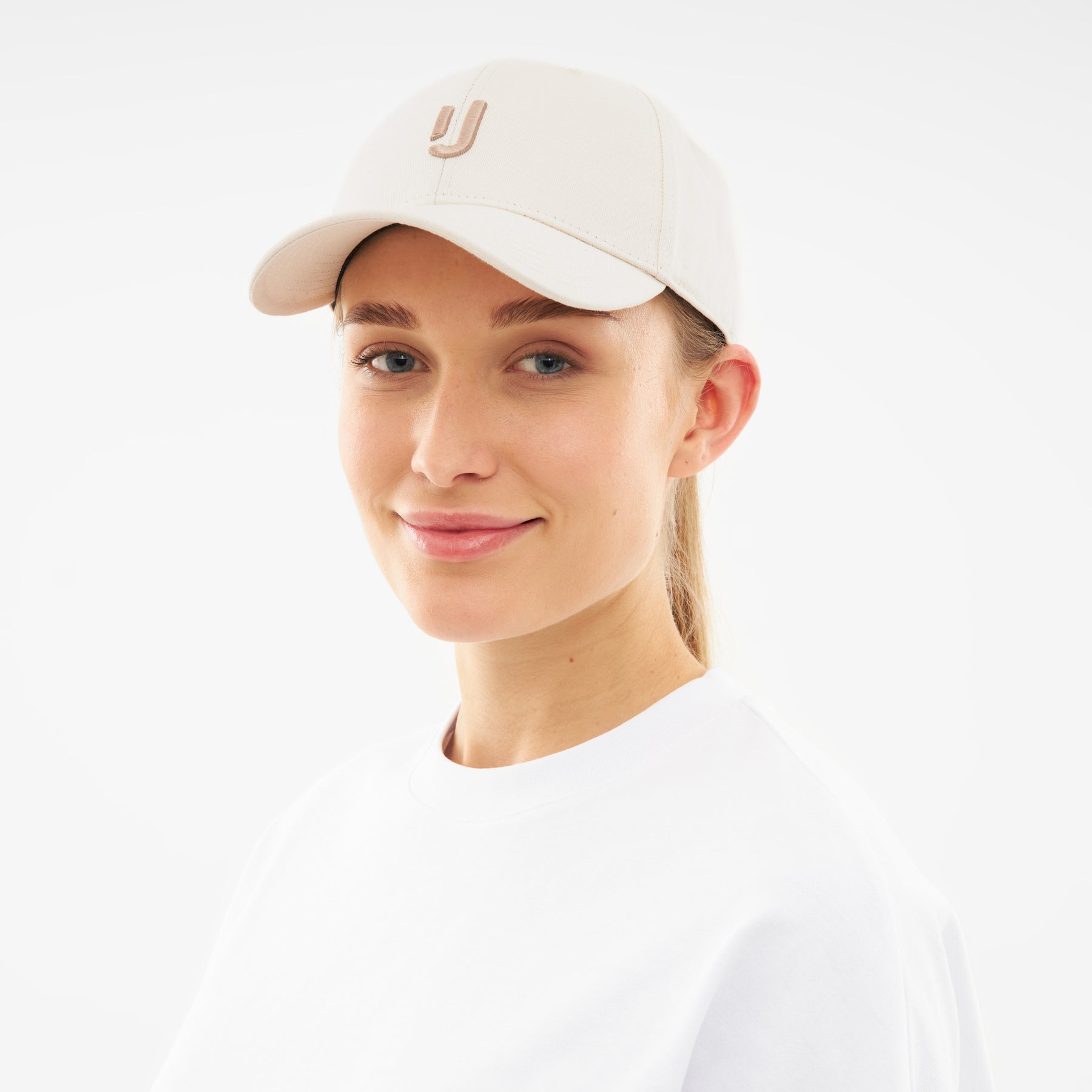 Frau trägt cremefarbene Cap 'Jason' mit Logo in dezentem Braun und weißem Oberteil