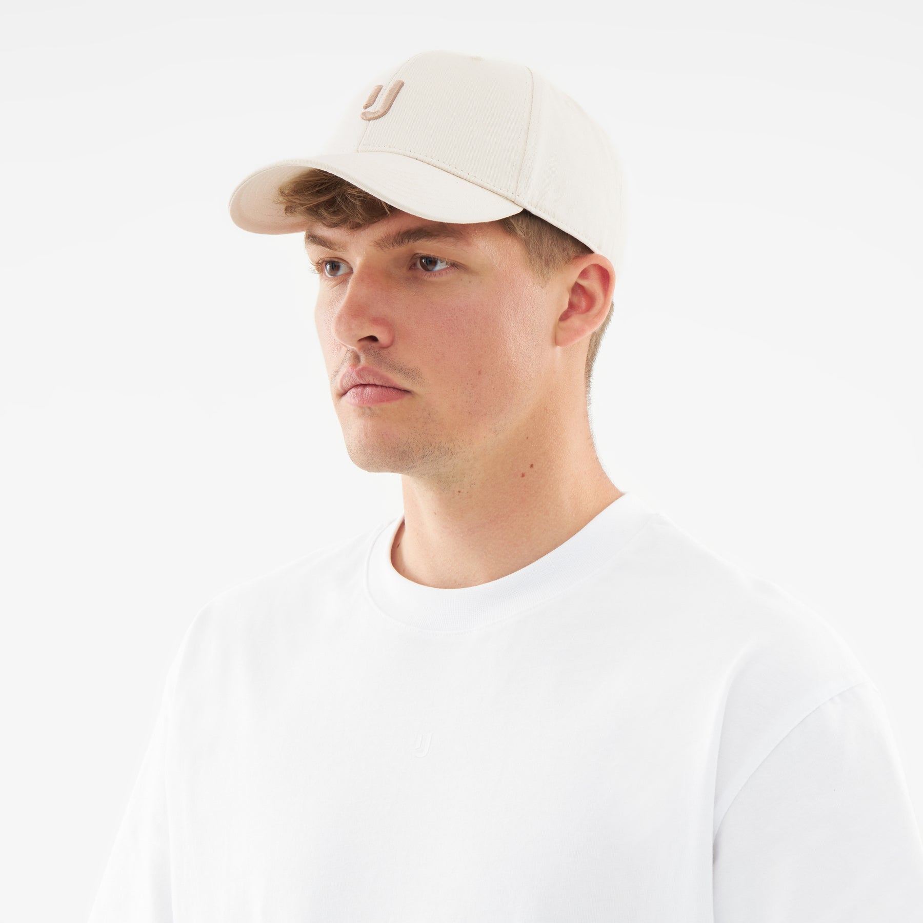 Mann trägt cremefarbene Snapback-Cap 'Jason' mit aufgesticktem J und weißes T-Shirt