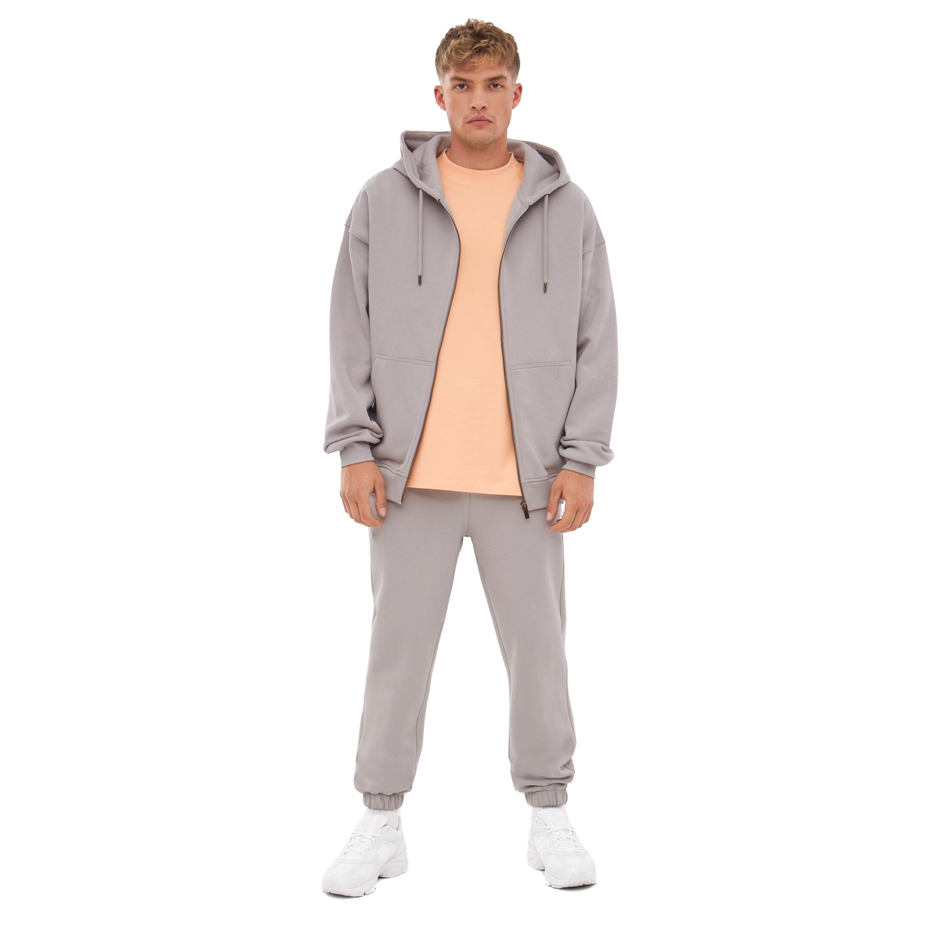 Mann trägt graue Jogginghose 'Owen', grauen Hoodie und helloranges T-Shirt