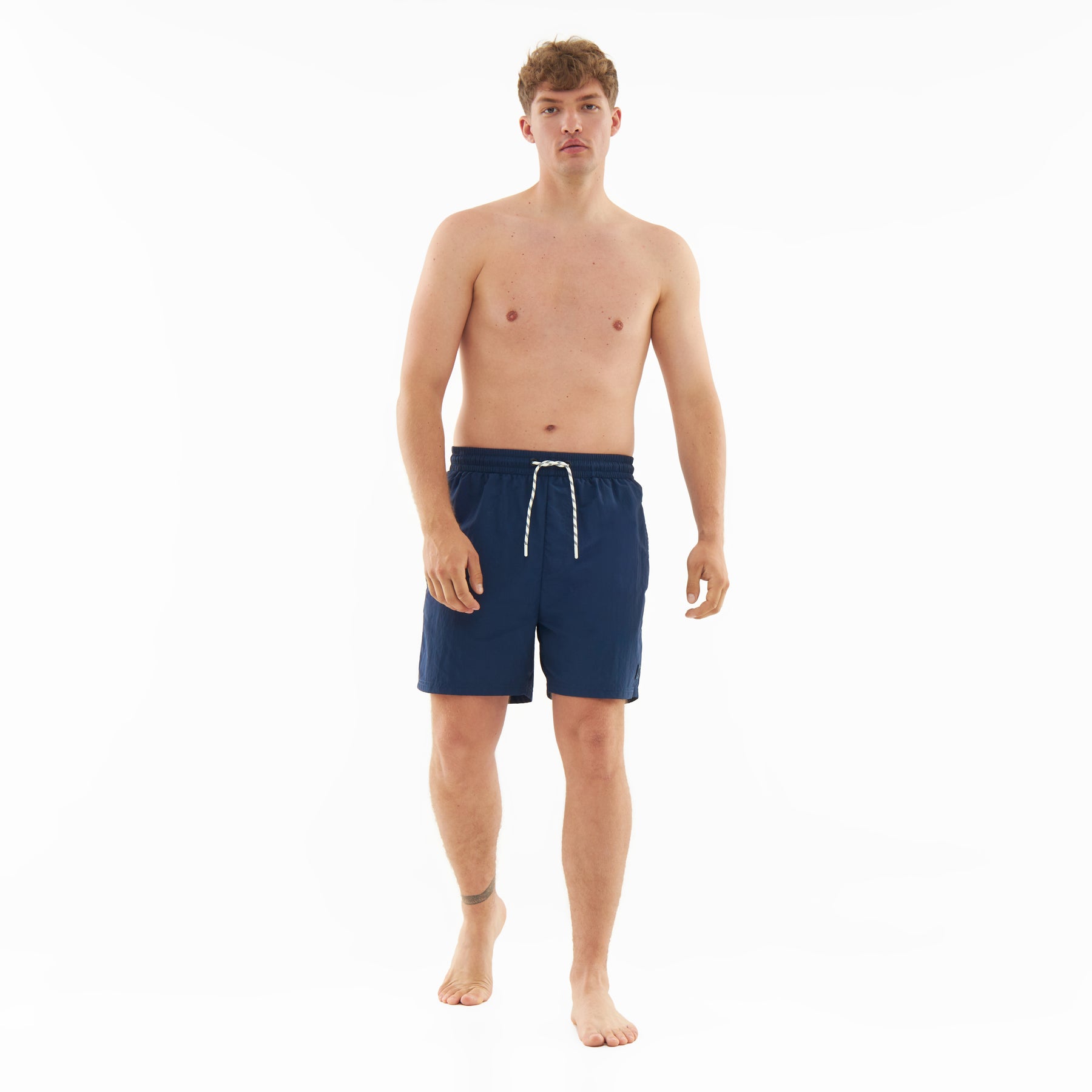 Mann trägt navyblaue Badehose 'Jay' mit weißem Kordelzug, barfuß vor weißem Hintergrund