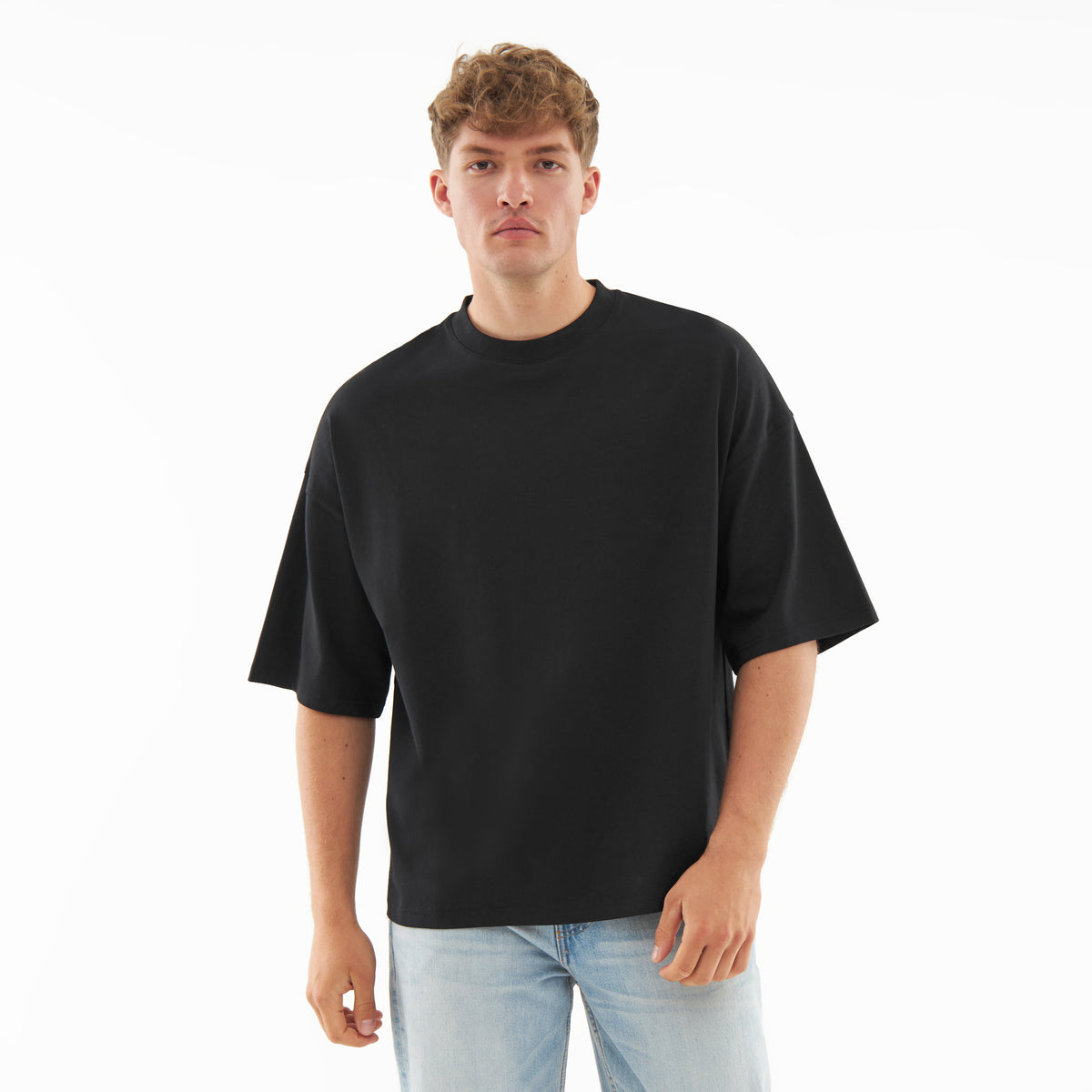 Mann trägt schwarzes T-Shirt 'Vic' mit lockerer Passform und kurzen Ärmeln, kombiniert mit hellblauen Jeans