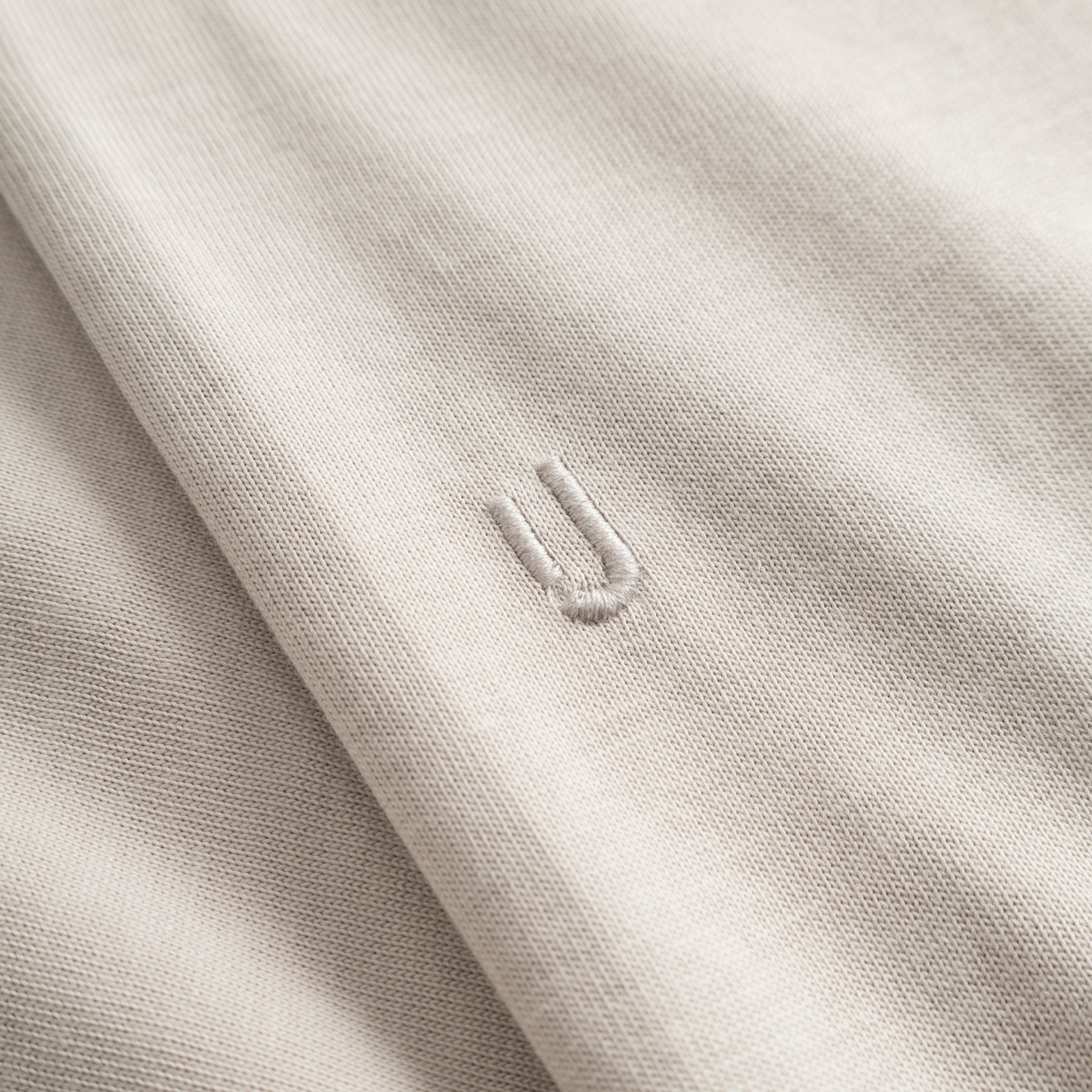 Nahaufnahme des beigen Stoffs eines Oversize-T-Shirts 'Vic' mit eingesticktem Detail