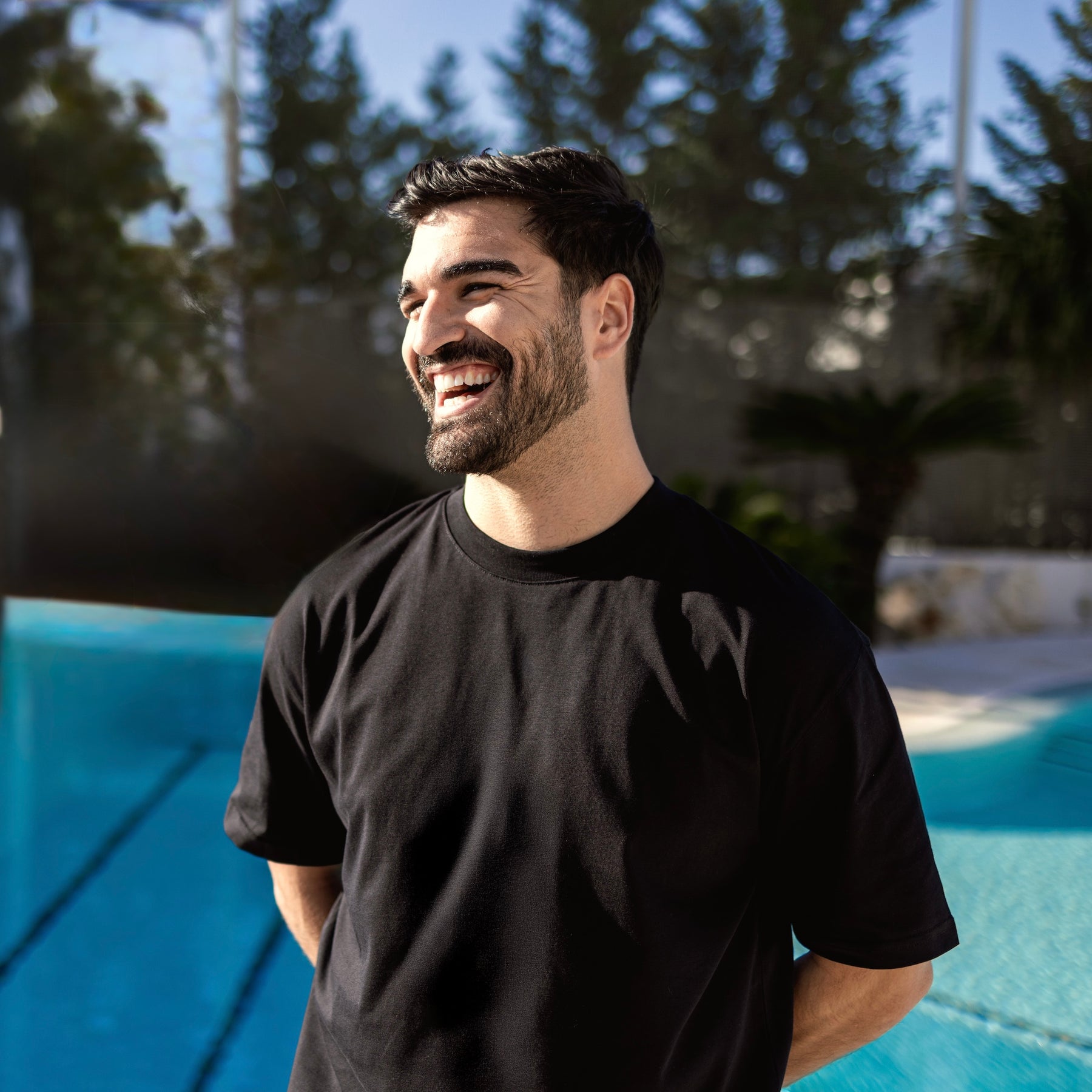 Mann trägt schwarzes Oversize-T-Shirt 'Vic' vor einem Pool